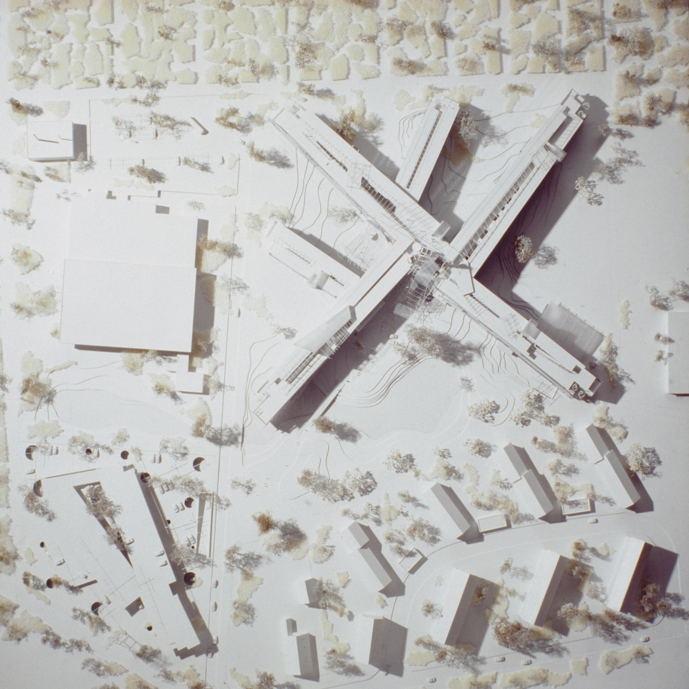 Project by Behnisch Architekturbuero, LVA &ndash; Landesversicherungsanstalt Schleswig-Holstein. Top-down view of an architectural model showing the cross-shaped building with surrounding streets, smaller buildings, and trees.