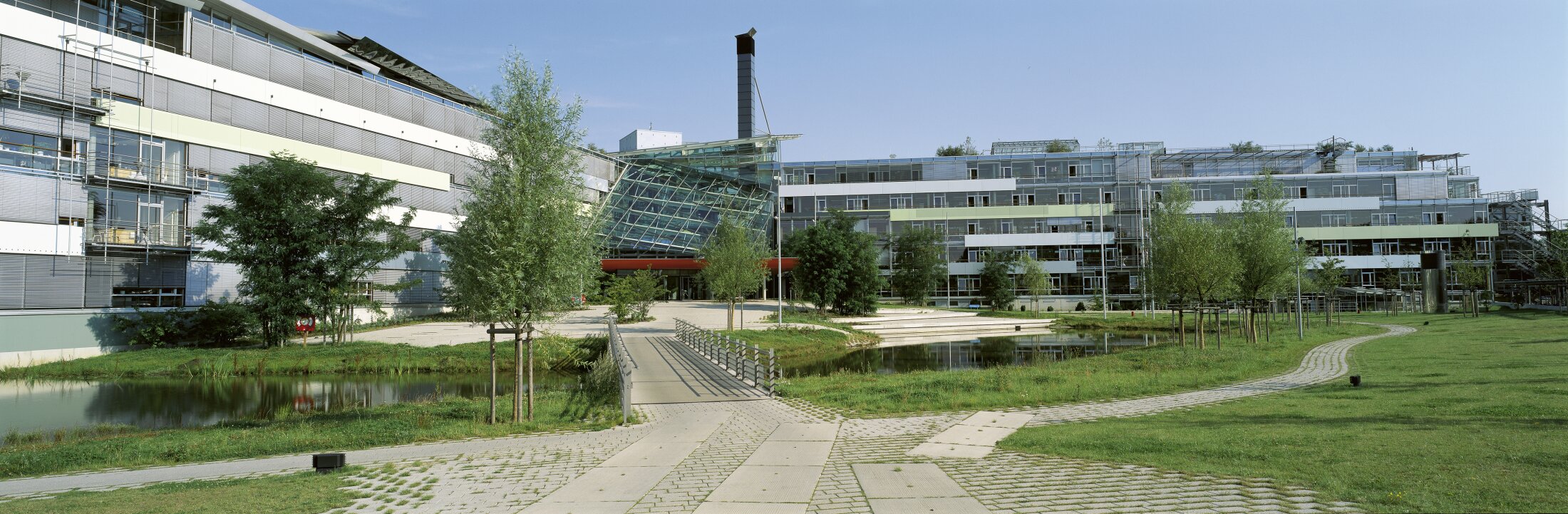 Project by Behnisch Architekturbuero, LVA &ndash; Landesversicherungsanstalt Schleswig-Holstein. Modern office complex with glass buildings, a landscaped park, ponds, trees, and a walkway leading to a central entrance.