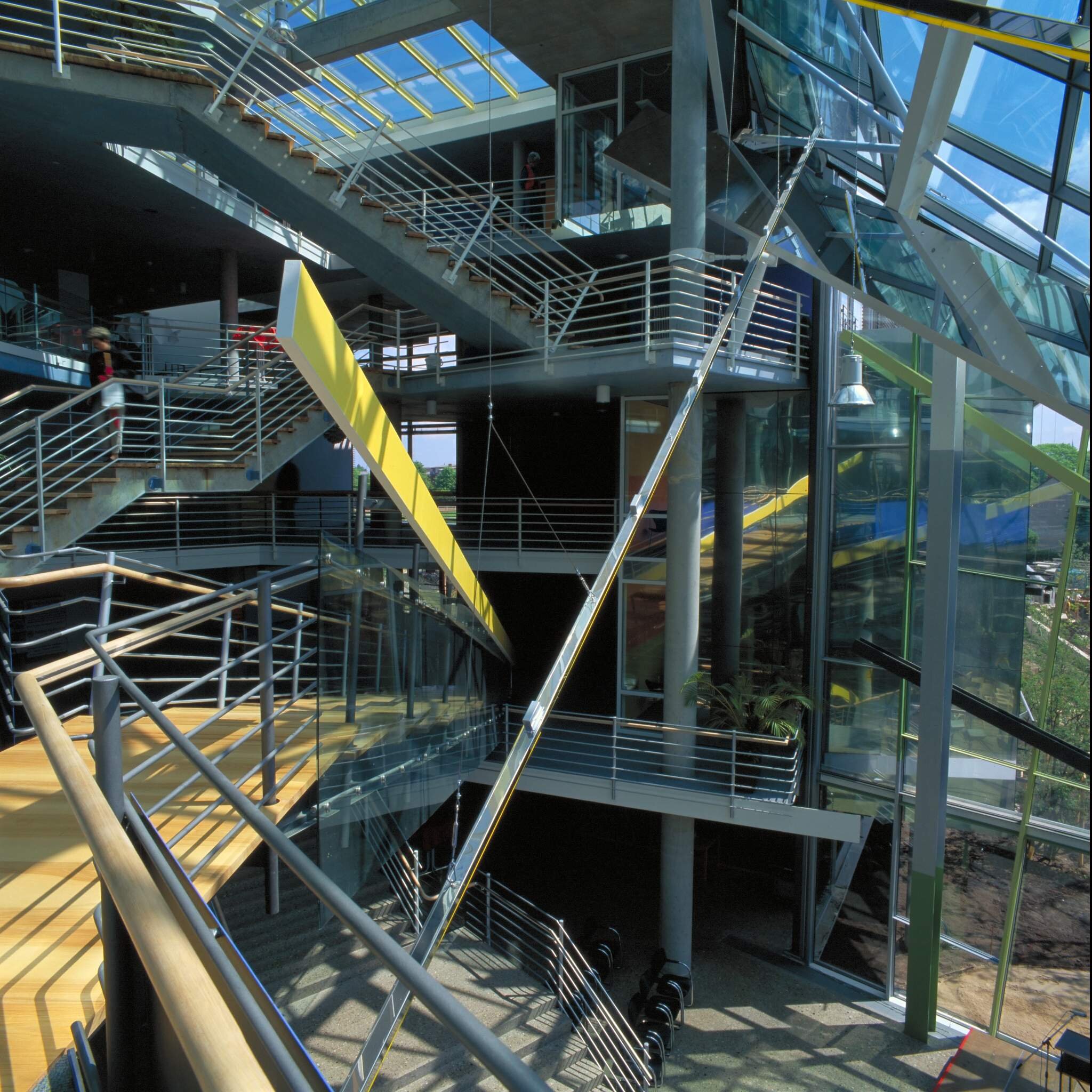 Project by Behnisch Architekturbuero, LVA &ndash; Landesversicherungsanstalt Schleswig-Holstein. Interior of the modern building with multiple staircases, glass walls, metal railings, and a skylight illuminating the space.