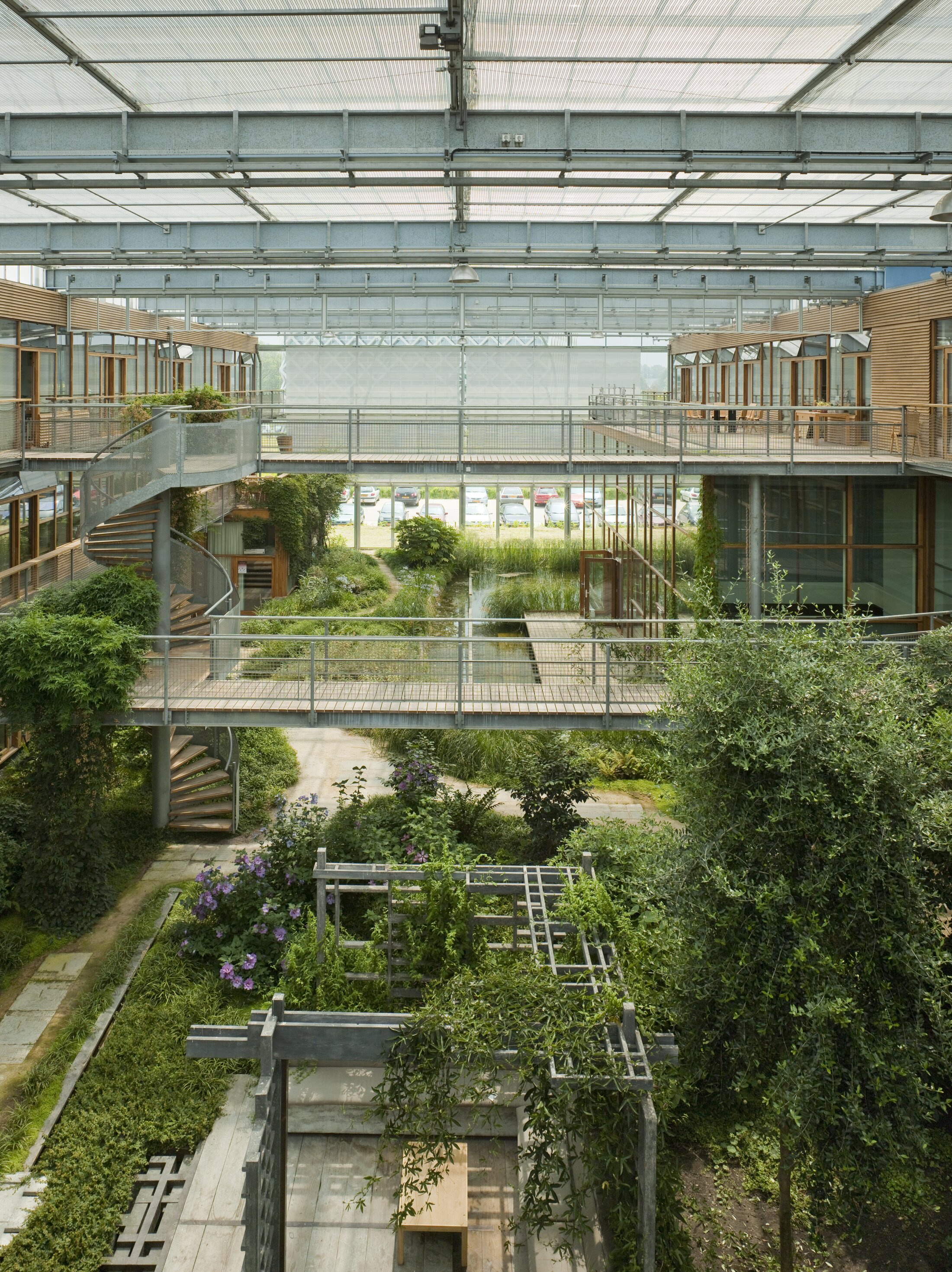 Project by Behnisch Architekturbuero, IBN-Institute for Forestry and Nature Research. Indoor atrium with lush plants, pathways, and water features, surrounded by glass-fronted offices and connected by bridges and staircases.