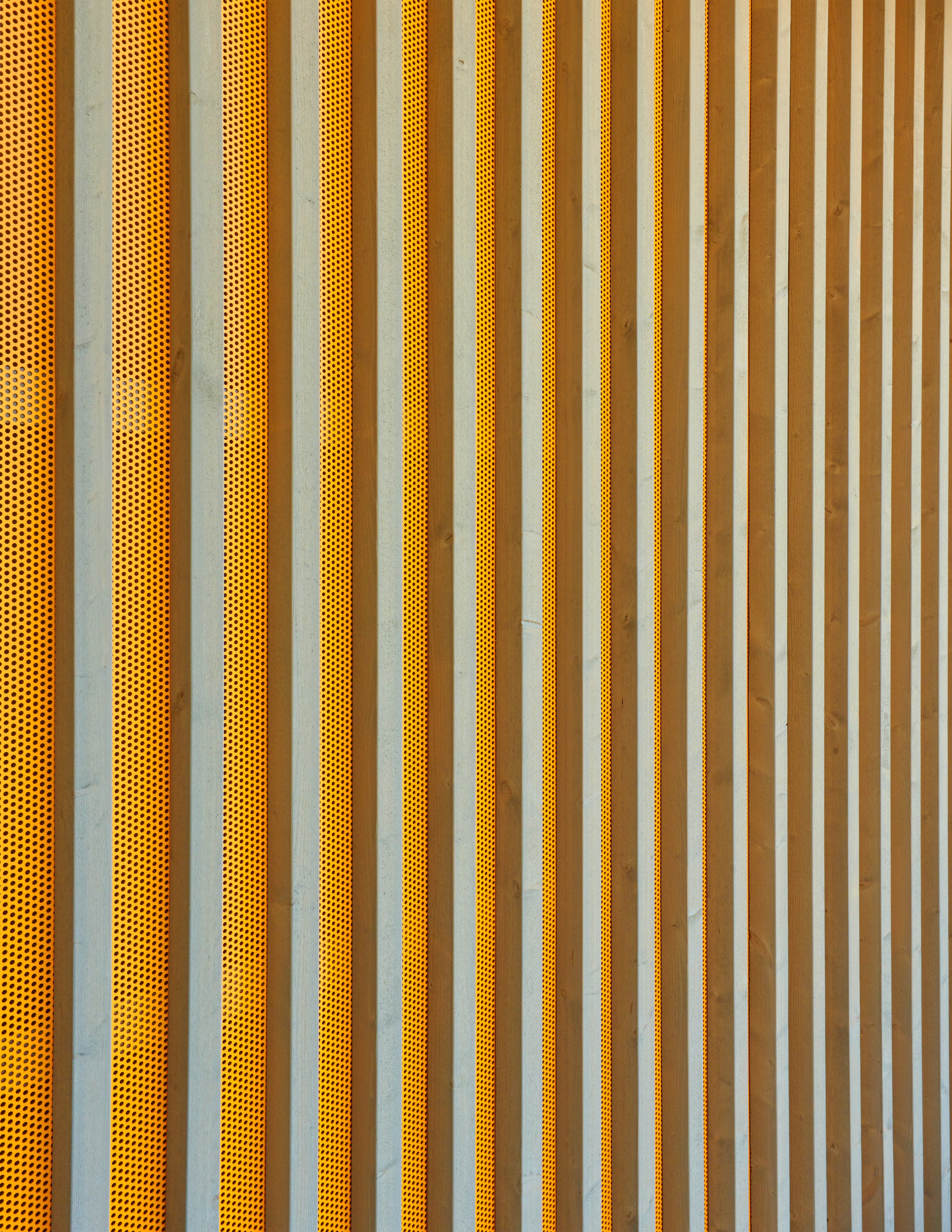 Project by Behnisch Architekturbuero, Gotthard-M&uuml;ller-School Bernhausen. Close-up of the facade with vertical slats alternating with perforated orange panels, creating a repeating striped pattern.