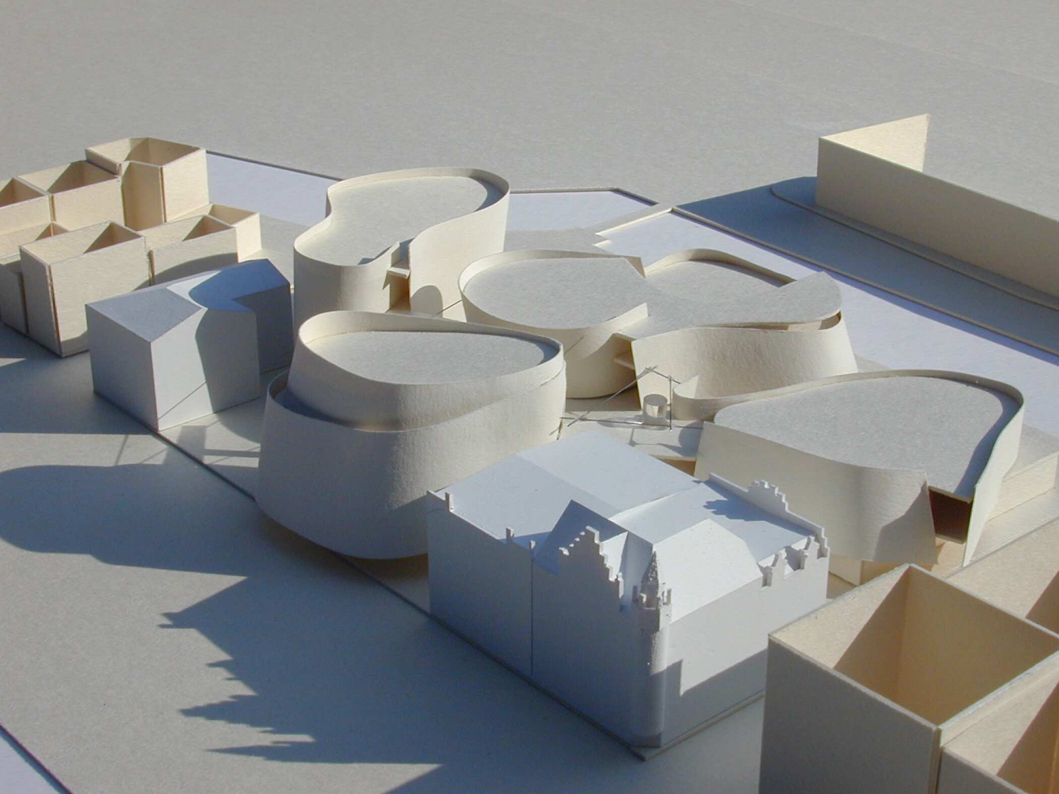 Project by Behnisch Architekturbuero, Ozeaneum. White architectural model with several rounded building forms arranged among block-like structures on a flat base.