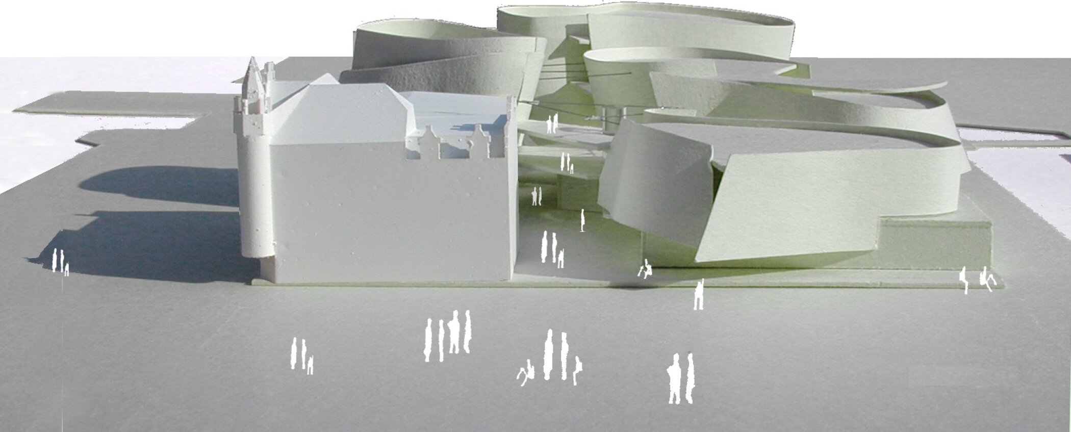 Project by Behnisch Architekturbuero, Ozeaneum. Architectural model showing a historic building beside curved modern structures, with pathways and small human figures for scale.