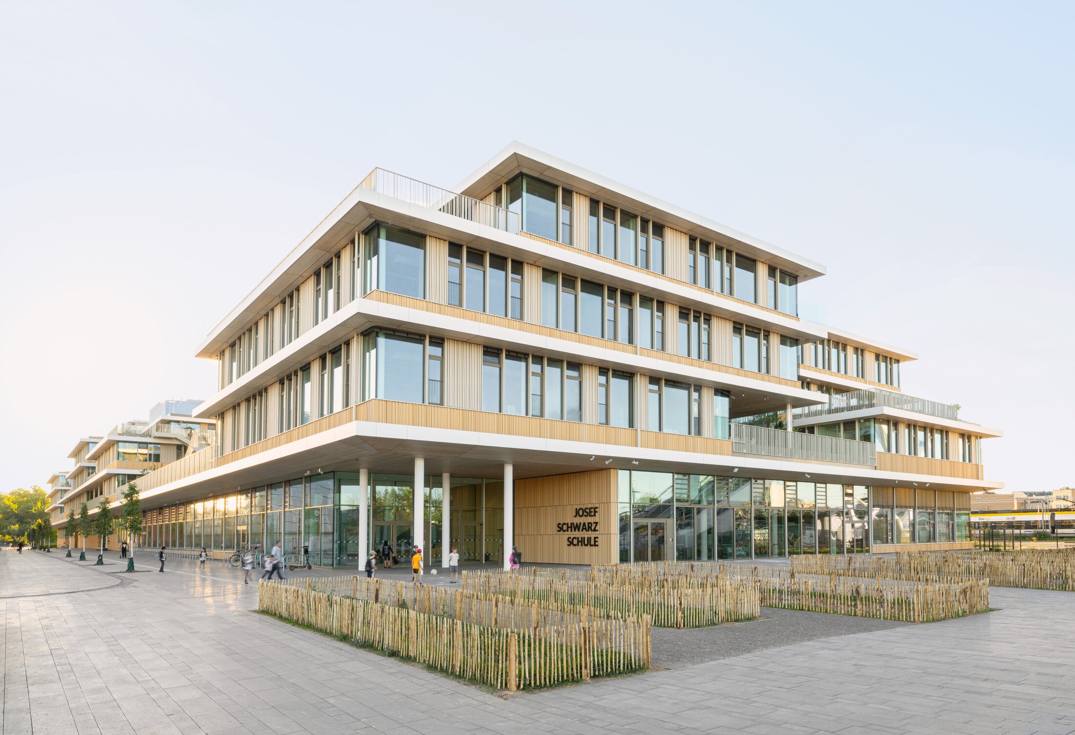 Project by Behnisch Architekturbuero, Josef-Schwarz School. Modern multi-story school building with wood facade and large windows. Some of the students playing outside in front of the main entrance.
