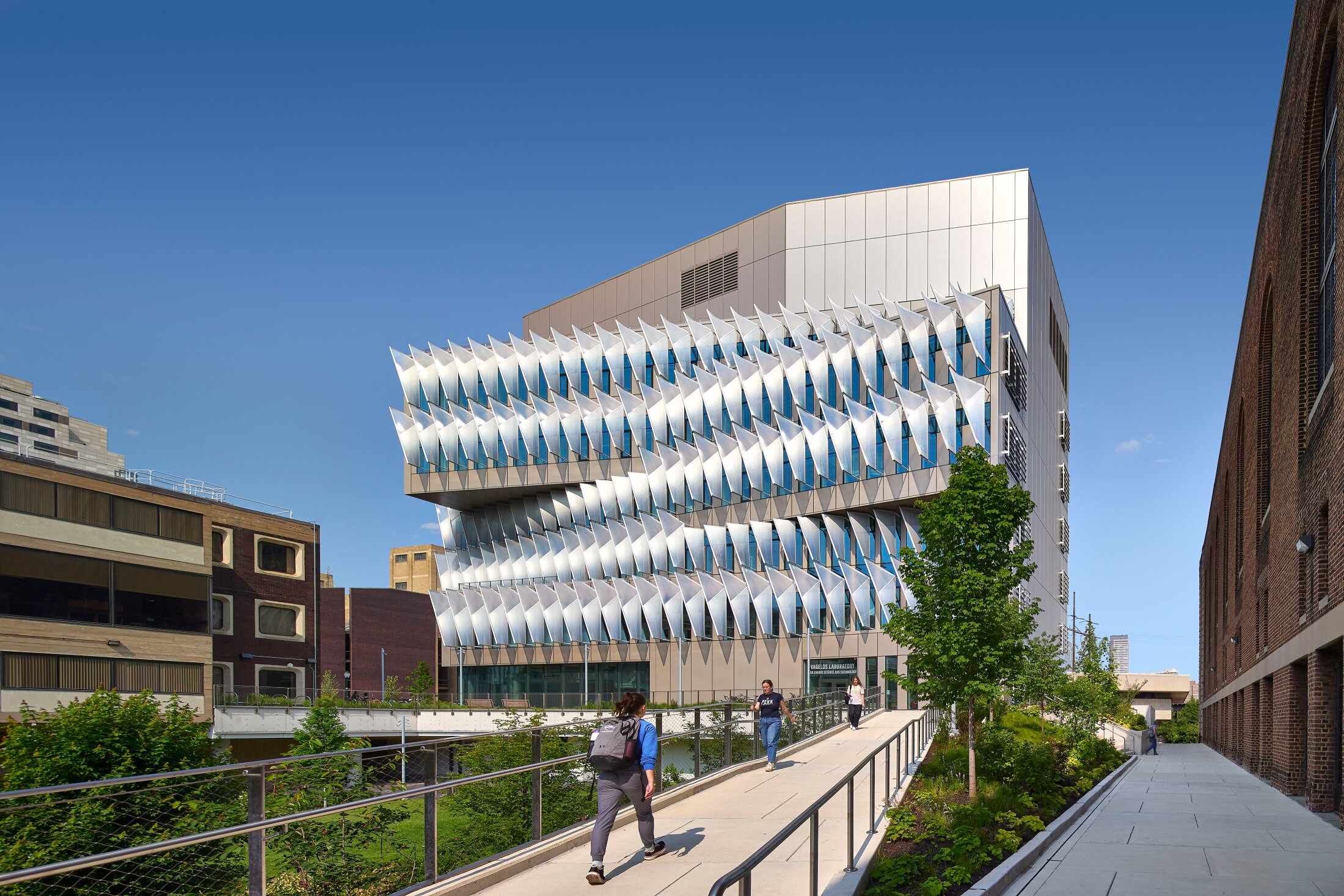Project by Behnisch Architekturbuero, The Vagelos Laboratory for Energy Science & Technology, University of Pennsylvania. Modern building with innovative sun protection. Pedestrians walk up the ramp to the building.