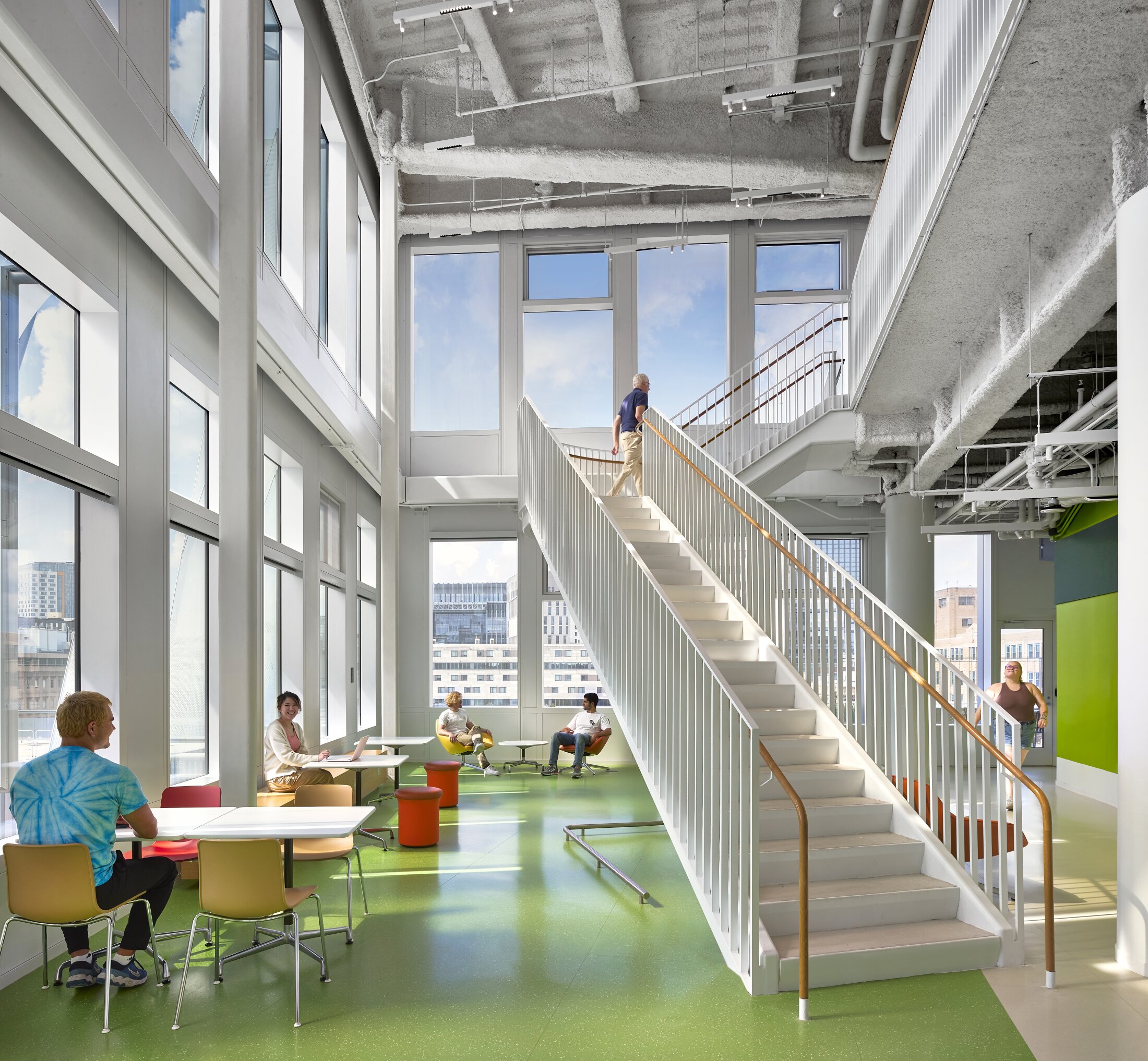 Project by Behnisch Architekturbuero, The Vagelos Laboratory for Energy Science & Technology, University of Pennsylvania. Bright atrium with a staircase leading up to the next floor, large windows, and people sitting and walking around in it.