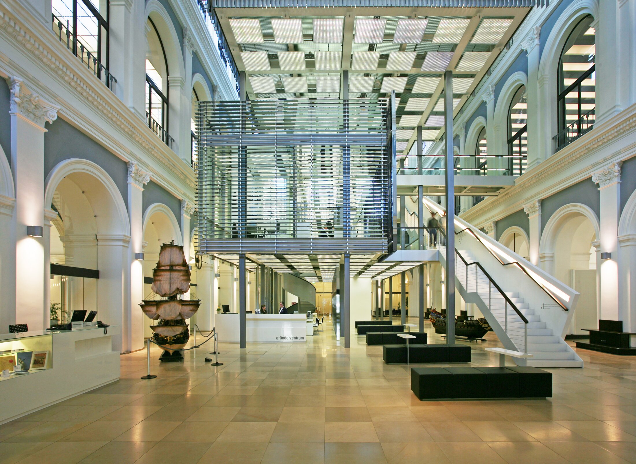 Project by Behnisch Architekturbuero, Haus im Haus. Large entrance area with curved walls, central glass meeting cube, reception desk, seating areas and a staircase leading to the upper levels.