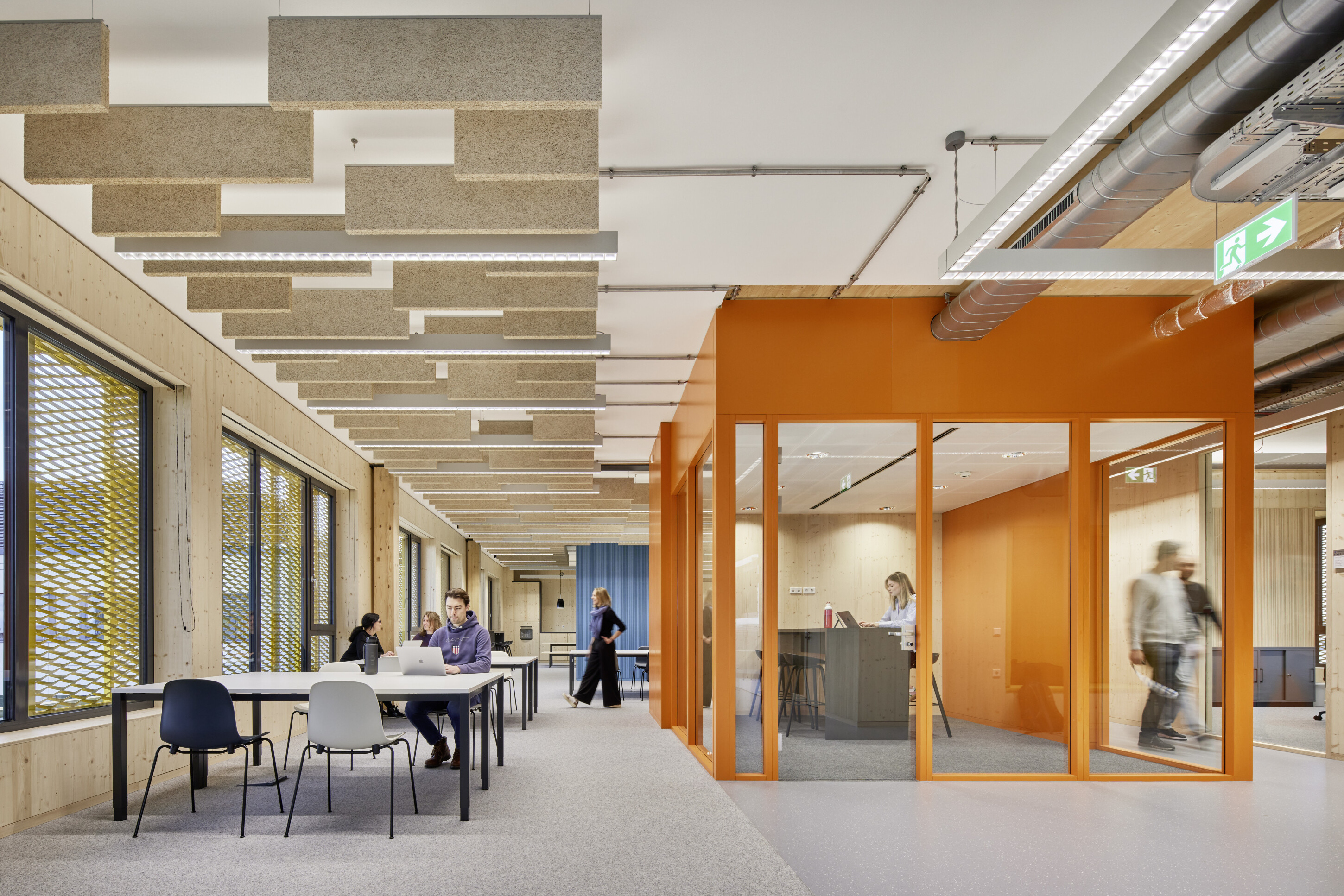 Project by Behnisch Architekturbuero, Extension Fachhochschulzentrum Münster University of Applied Sciences. Open office interior with desks, people working, and an open orange meeting room with glass walls.