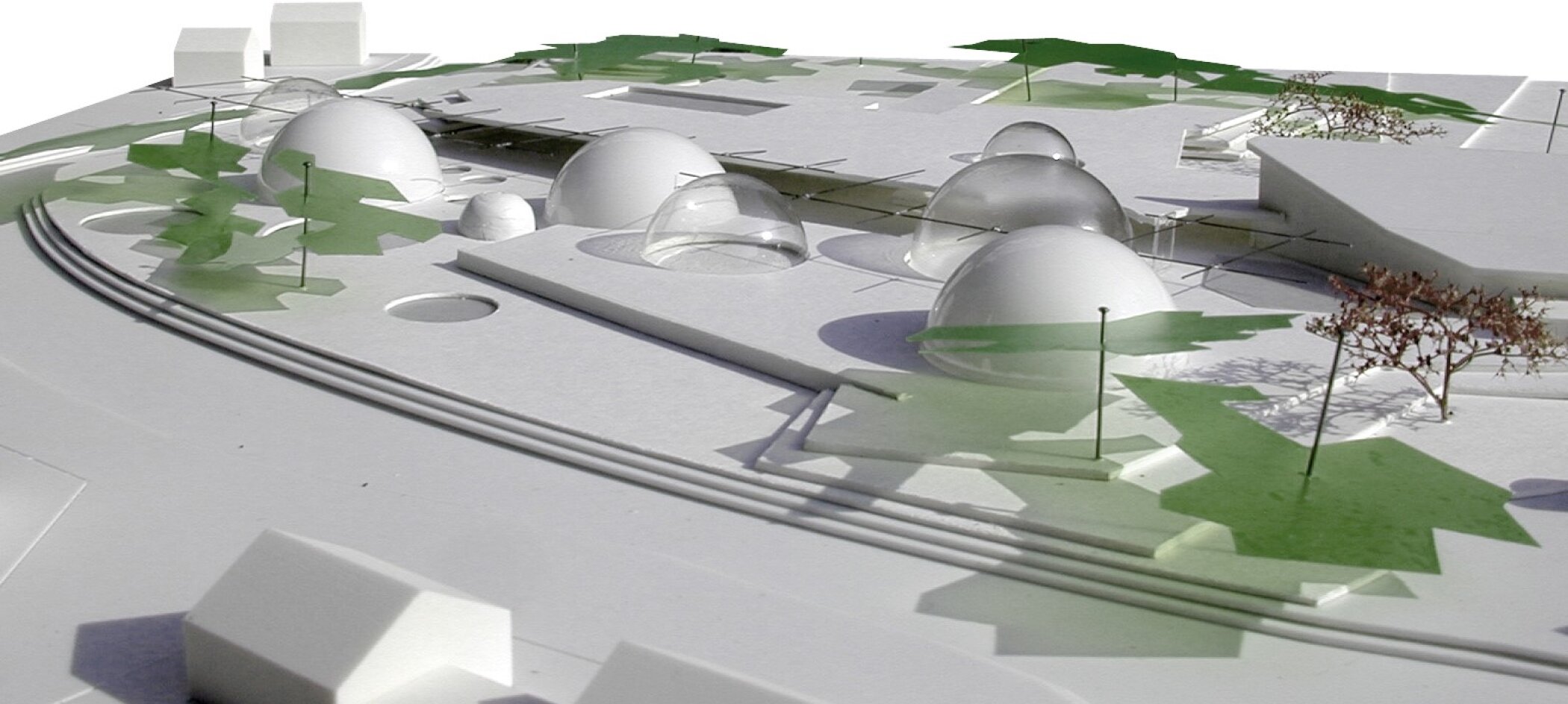 Project by Behnisch Architekturbuero, Thermal Spa Bad Aibling. White site model with low buildings and several domed structures, surrounded by abstract green areas indicating trees and landscape paths.