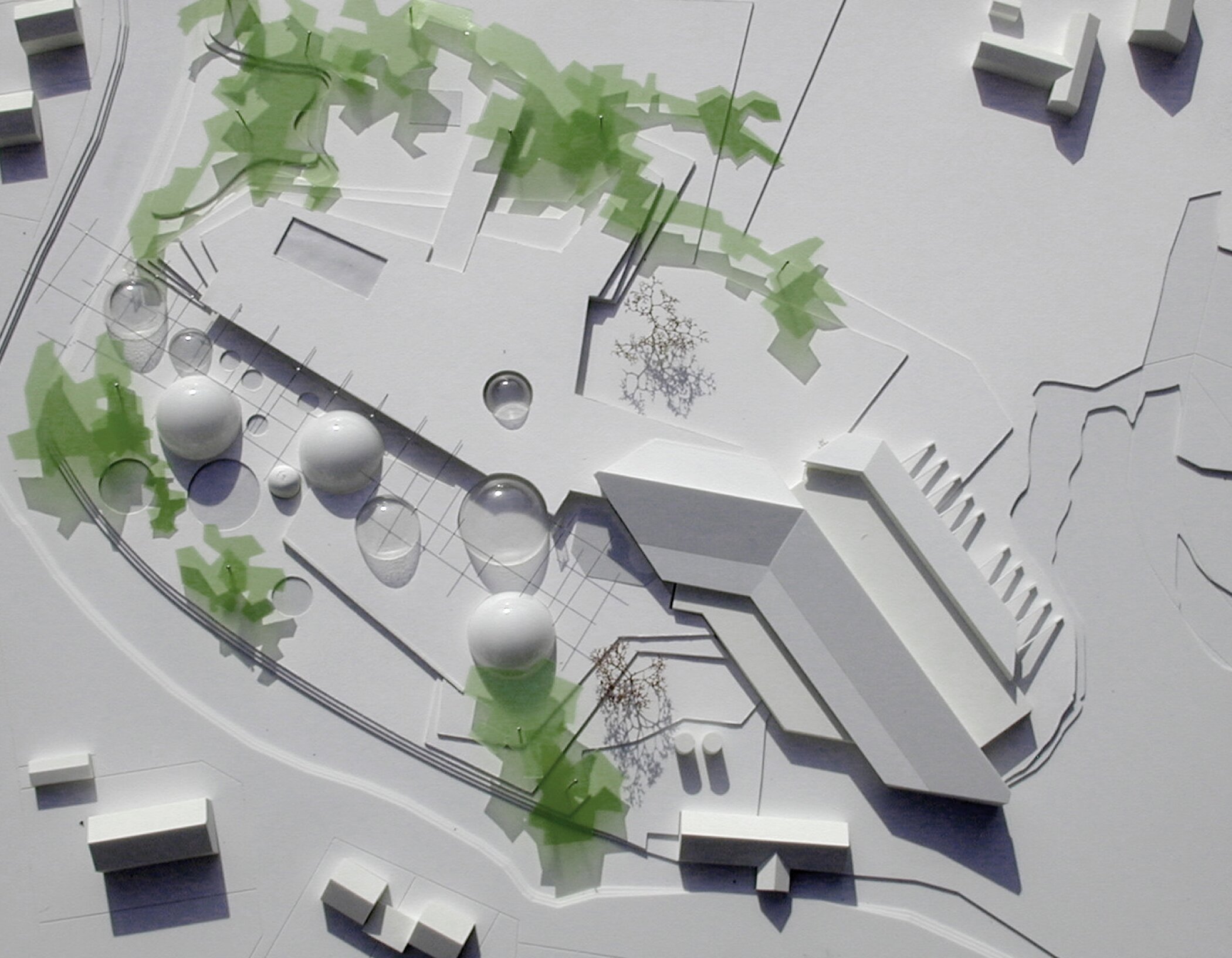 Project by Behnisch Architekturbuero, Thermal Spa Bad Aibling. White site model with low buildings and several domed structures, surrounded by abstract green areas indicating trees and landscape paths.