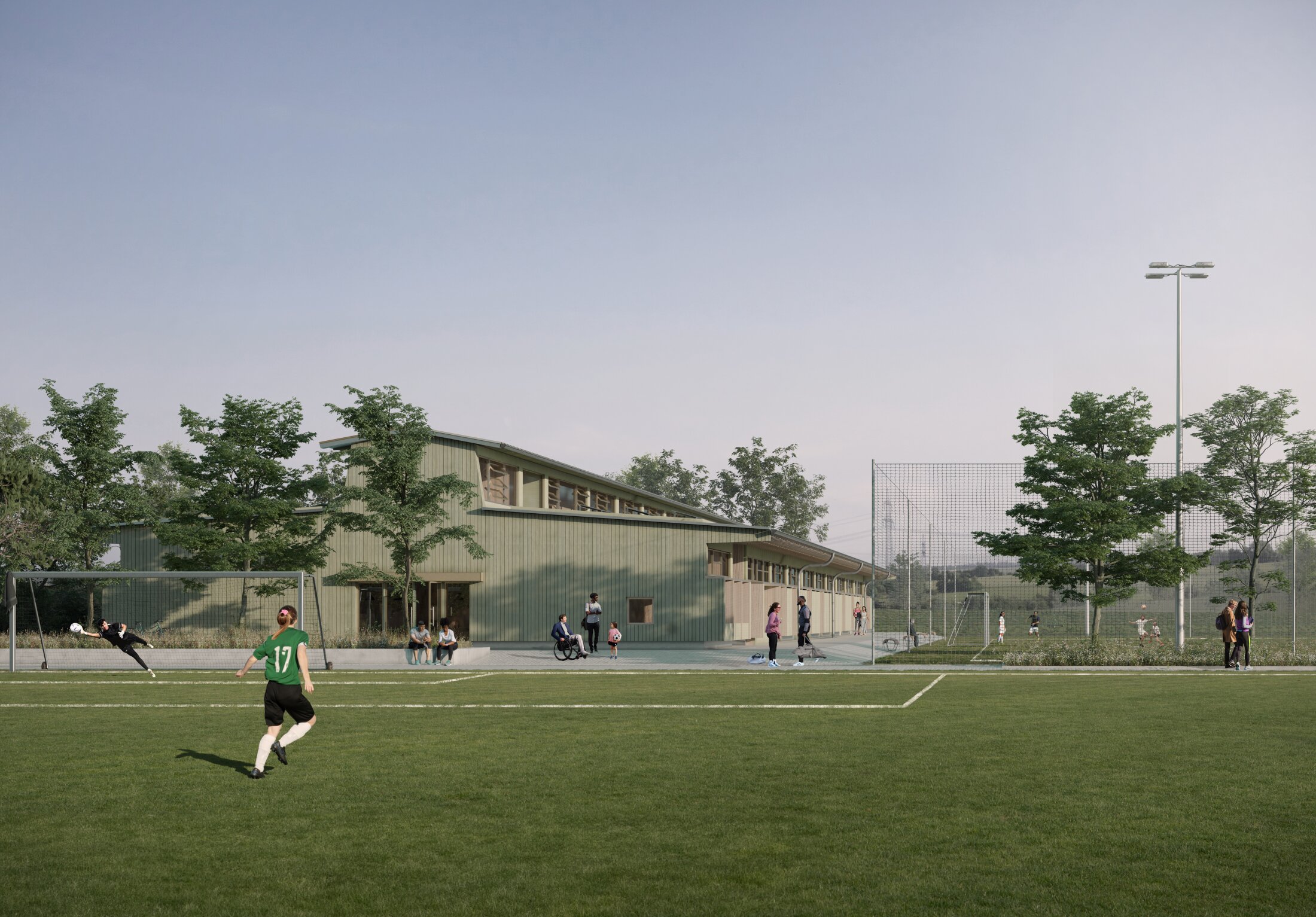 Project by Behnisch Architekturbuero, Juchhof. Soccer field with players in action, a goalkeeper diving, and a low building with trees and people standing nearby in the background.