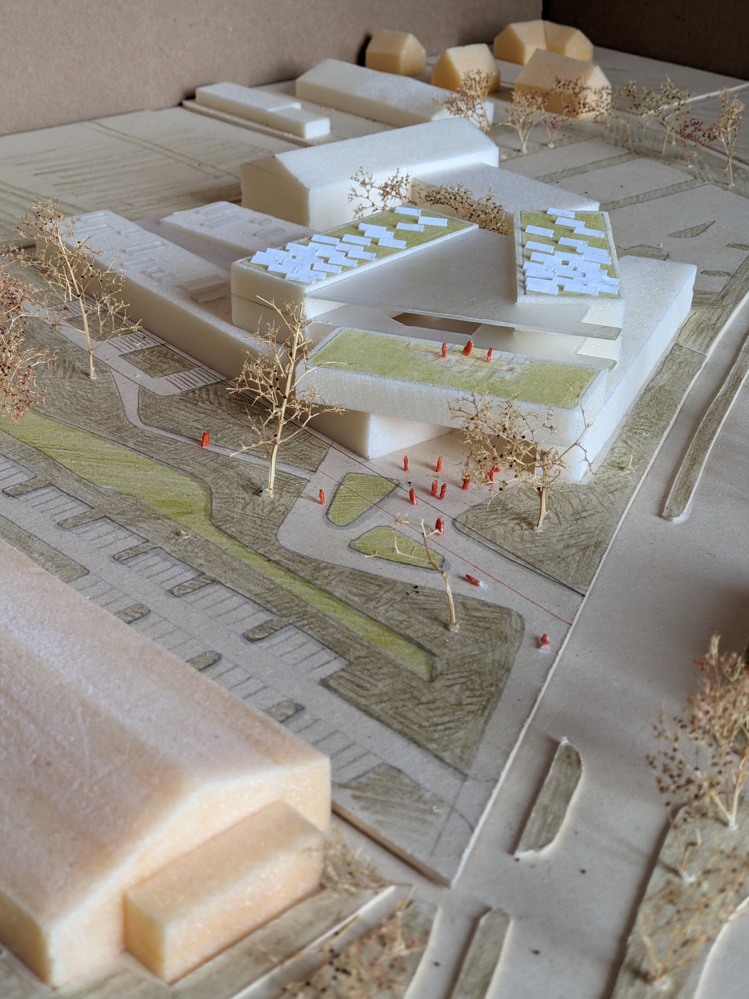 Project by Behnisch Architekturbuero, New Educational Center Handwerkskammer Niederbayern. Top view of an architectural model with a modern building, surrounding streets, trees, and small figures indicating people in the site layout.