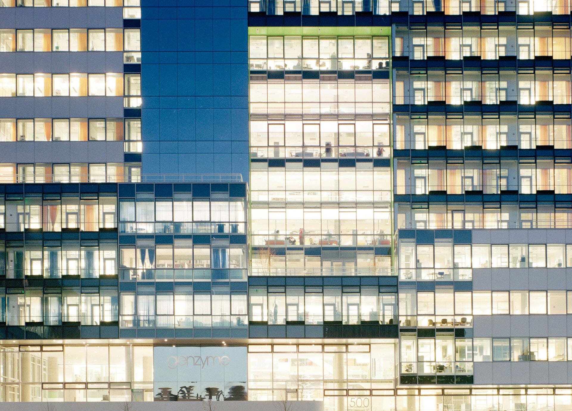 Project by Behnisch Architekturbuero, Genzyme Center.Close view of the illuminated office building facade at night, showing multiple floors with glass walls and visible interior workspaces.