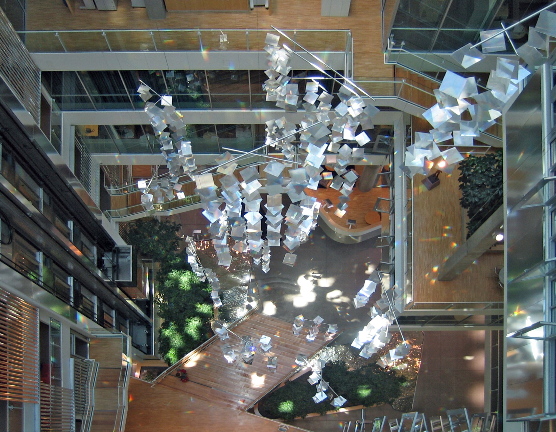 Project by Behnisch Architekturbuero, Genzyme Center. Overhead view of atrium with staircases, indoor greenery, and a suspended installation of the sunlight redirection system.