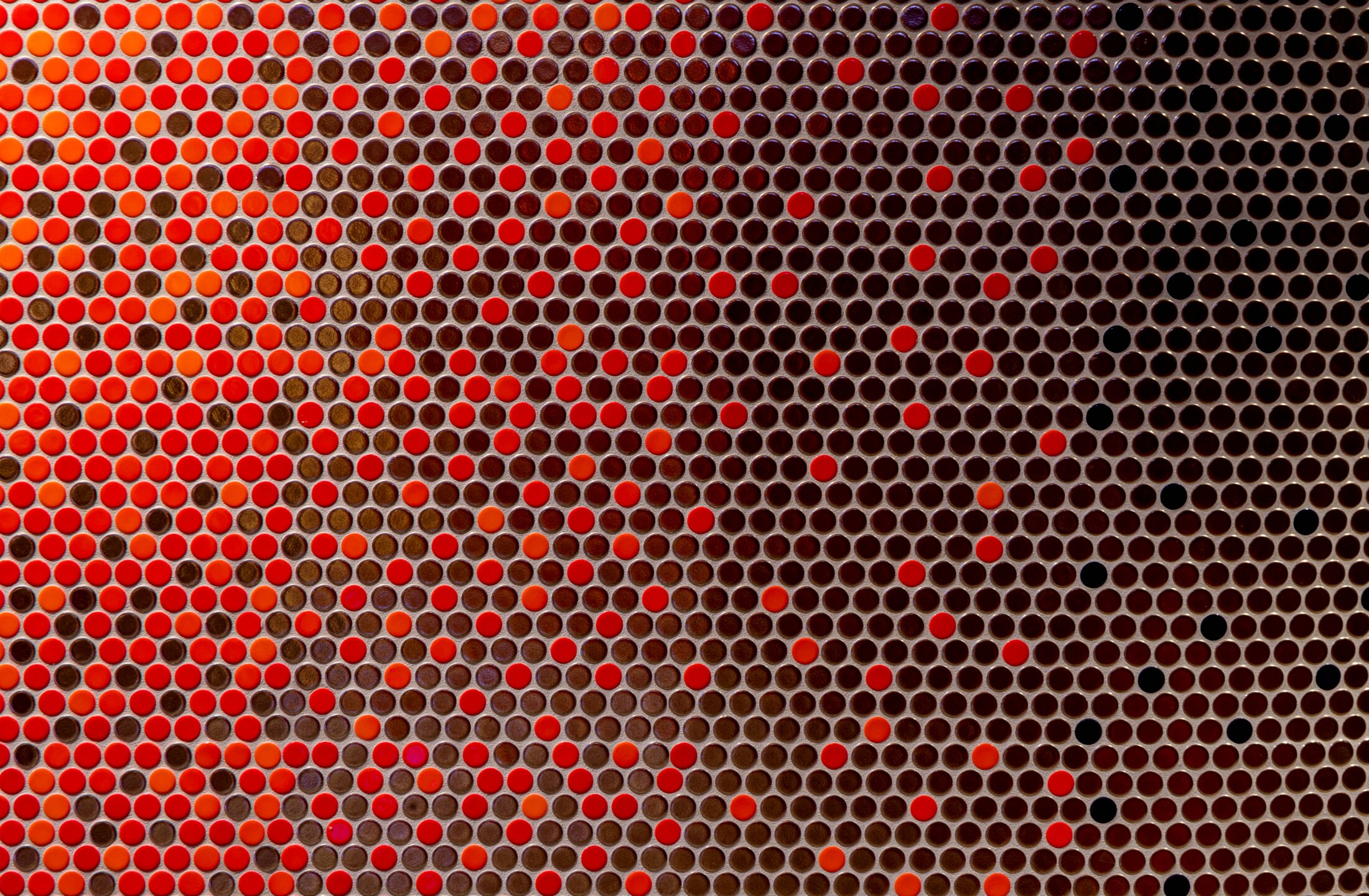 Project by Behnisch Architekturbuero, Sportbad Friedrichshafen. Close-up of the  surface covered with small circular tiles in shades of red, orange, brown, and black arranged in a dense pattern.
