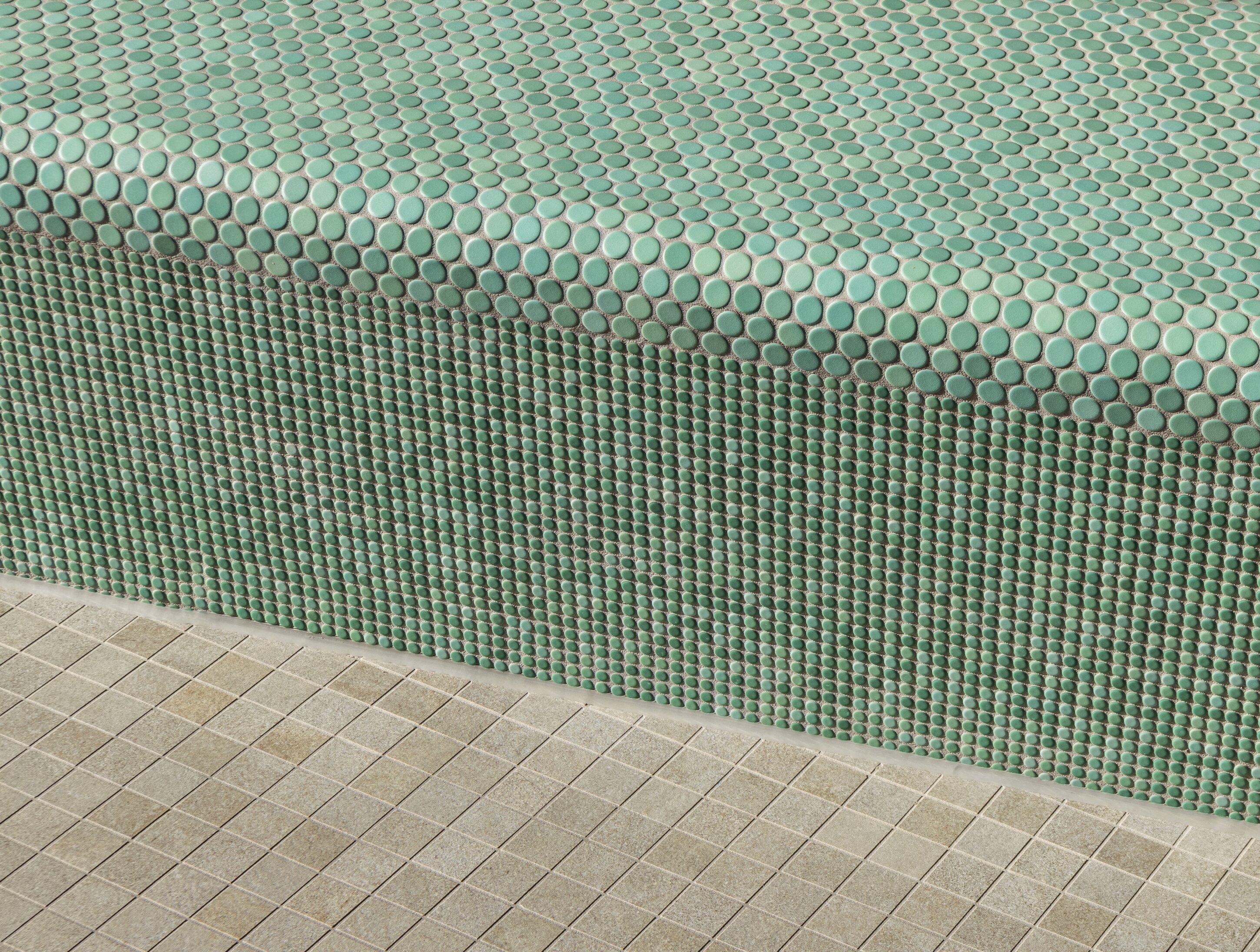 Project by Behnisch Architekturbuero, Sportbad Friedrichshafen. Green circular mosaic tiles covering a pool edge and wall, with beige square floor tiles in the foreground.