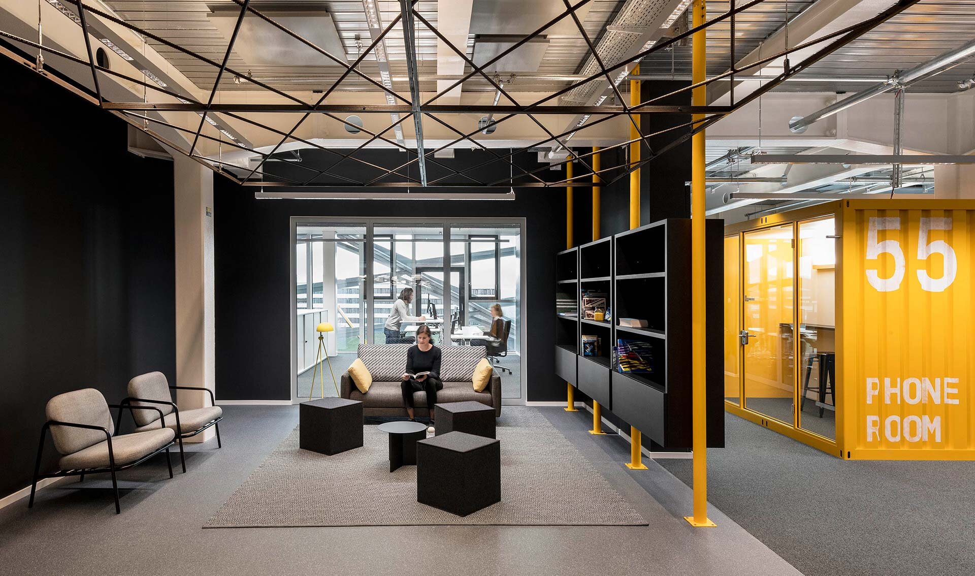 Project by Behnisch Architekturbuero, adidas ARENA. Modern office lounge with sofa seating and tables, glass meeting room behind, and yellow &ldquo;phone room&rdquo; booth on the right hand side.
