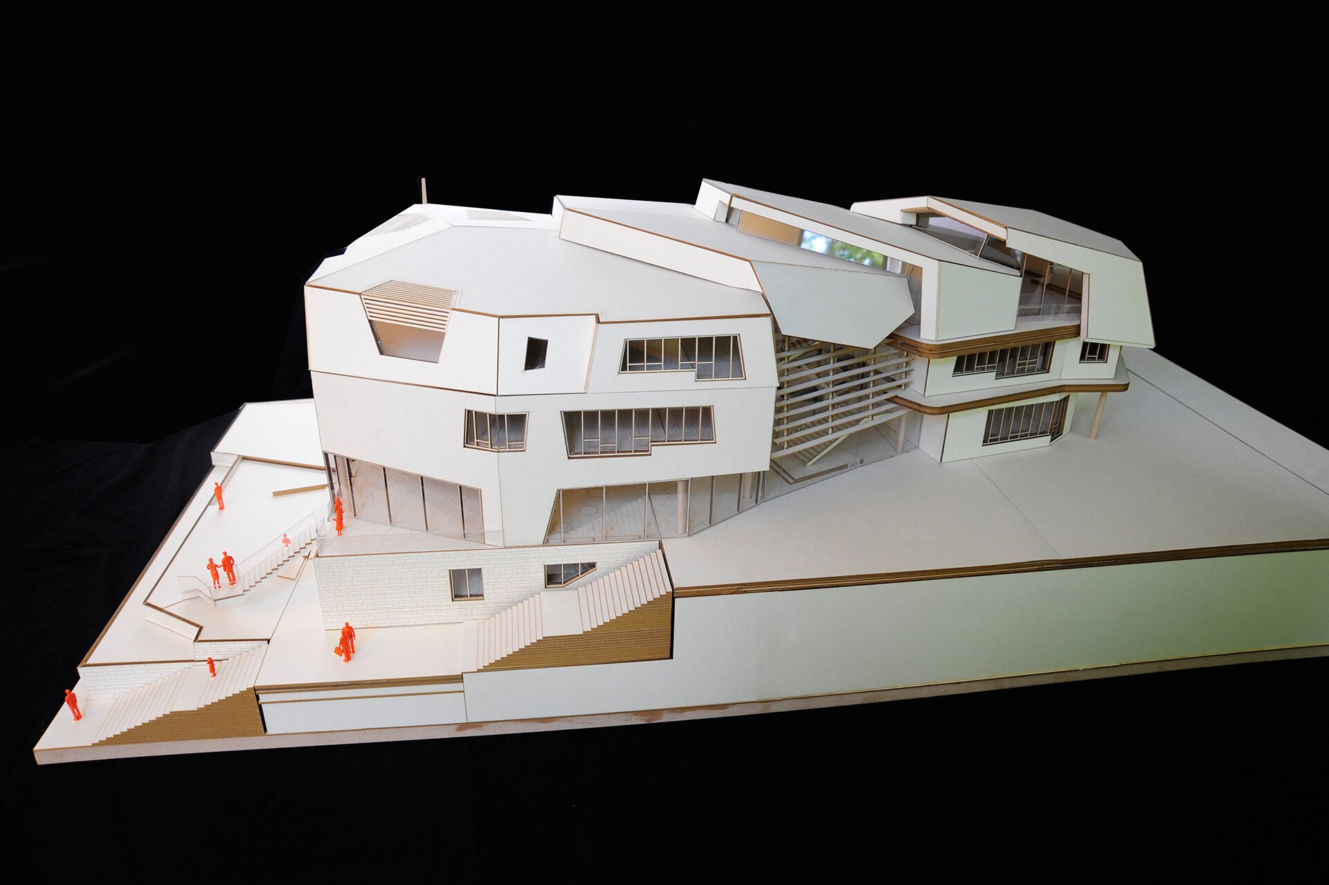Project by Behnisch Architekturbuero, Freie Waldorfschule Uhlandshoehe - New School and Administration Building. Architectural scale model of the multi-level building with angular forms, stairs, and small orange human figures on a sloped site.