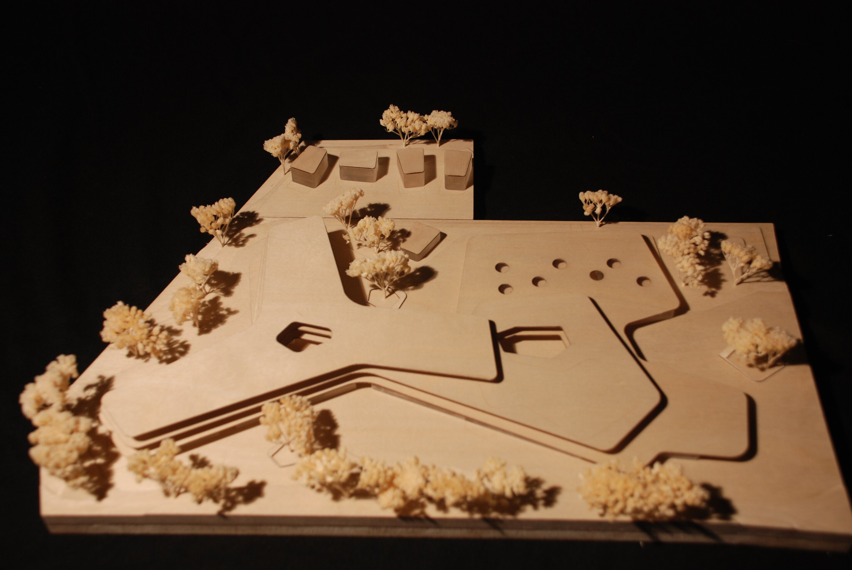 Project by Behnisch Architekturbuero, Lurup Neighborhood School. Architectural site model with buildings, paths, and small trees arranged on a base, shown against a dark background.