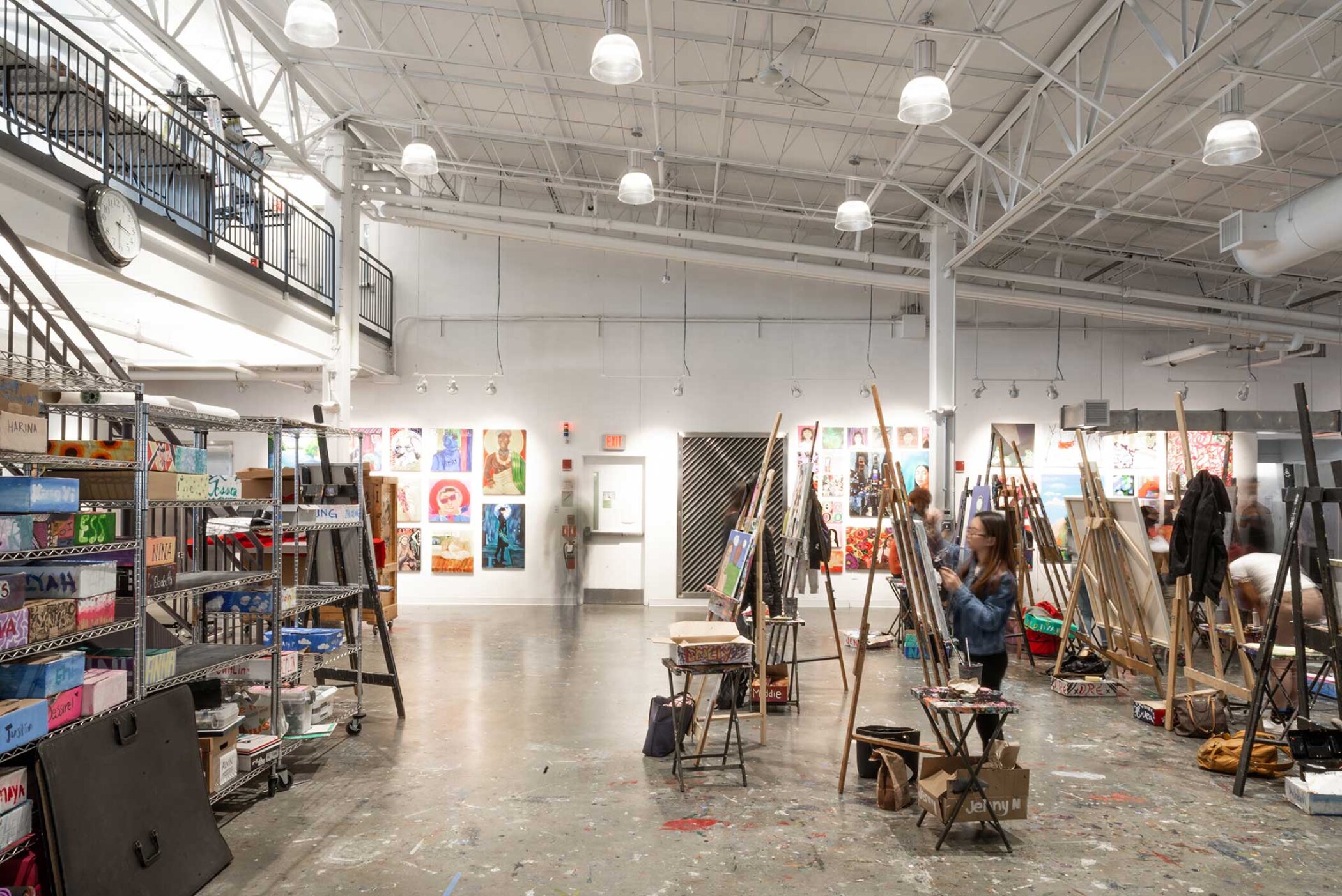 Project by Behnisch Architekturbuero, Artists for Humanity EpiCenter Expansion. Spacious art studio with high ceilings, easels and supplies, people painting, and colorful artworks displayed on the walls.