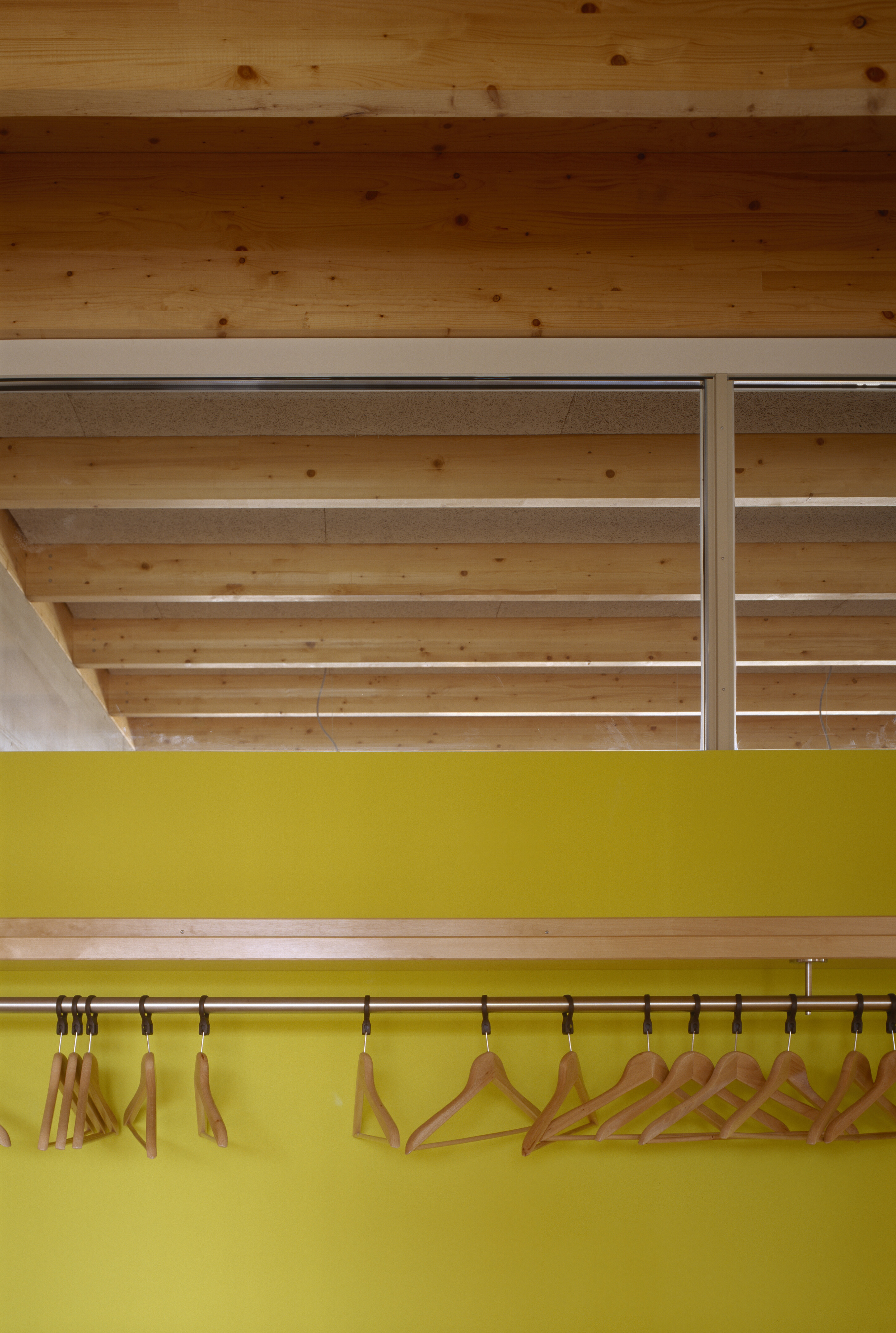 Project by Behnisch Architekturbuero, Pistorius School Herbrechtingen. Row of wooden coat hangers on a rail against a yellow wall, with a wood-beamed ceiling visible above.