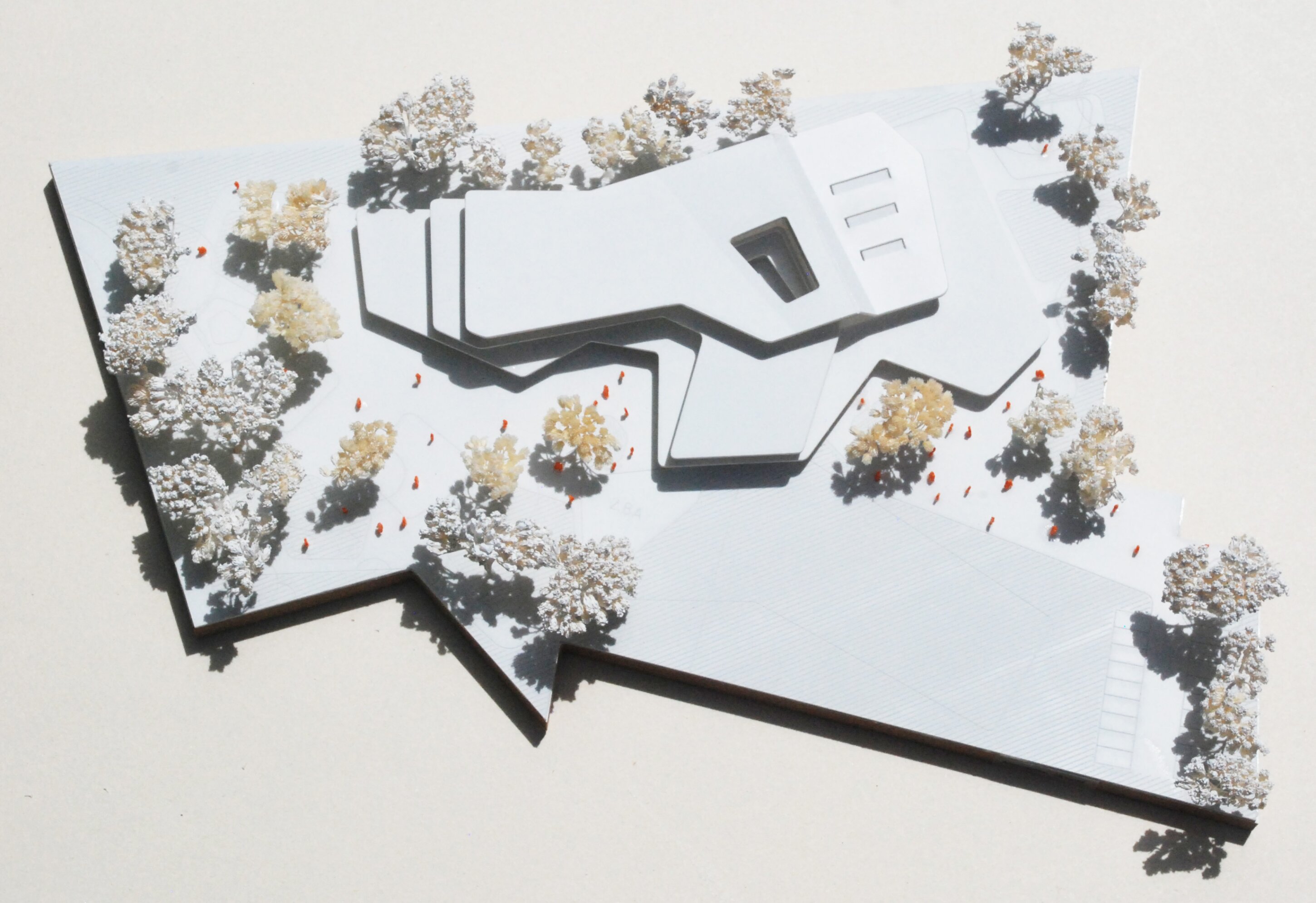Project by Behnisch Architekturbuero, Ludwig-Weber School. Top view of an architectural model showing a multi-wing building surrounded by miniature trees and small figures on a site layout.