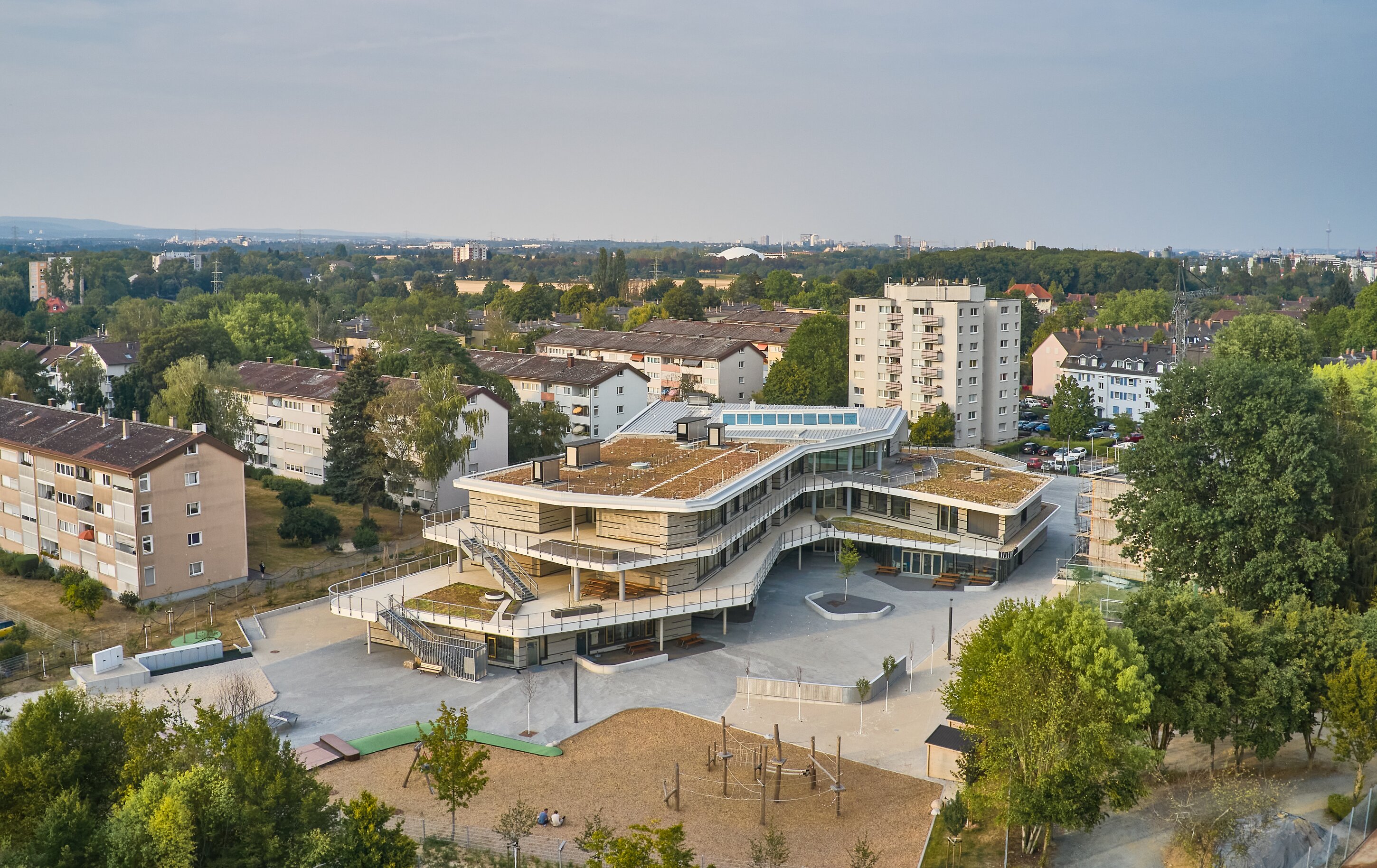 Project by Behnisch Architekturbuero, Ludwig-Weber School. Aerial view of the school complex with green roofs, courtyard and playground, surrounded by residential buildings and trees.