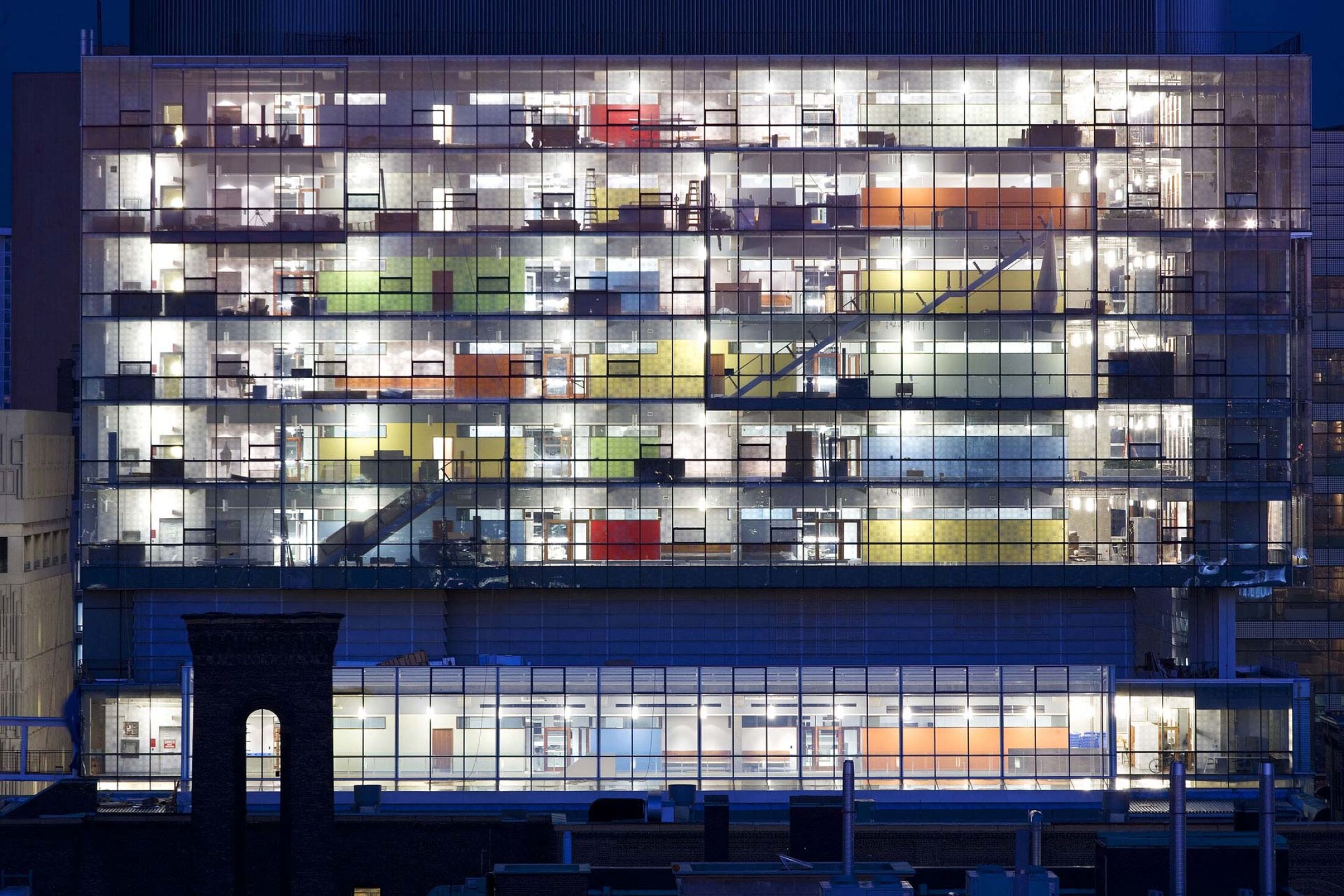 Project by Behnisch Architekturbuero, The Donnelly Centre for Cellular and Biomolecular Research. Night shot of the multi-story office building with a glass facade, whose brightly lit floors reveal interiors, staircases and colorful wall surfaces.