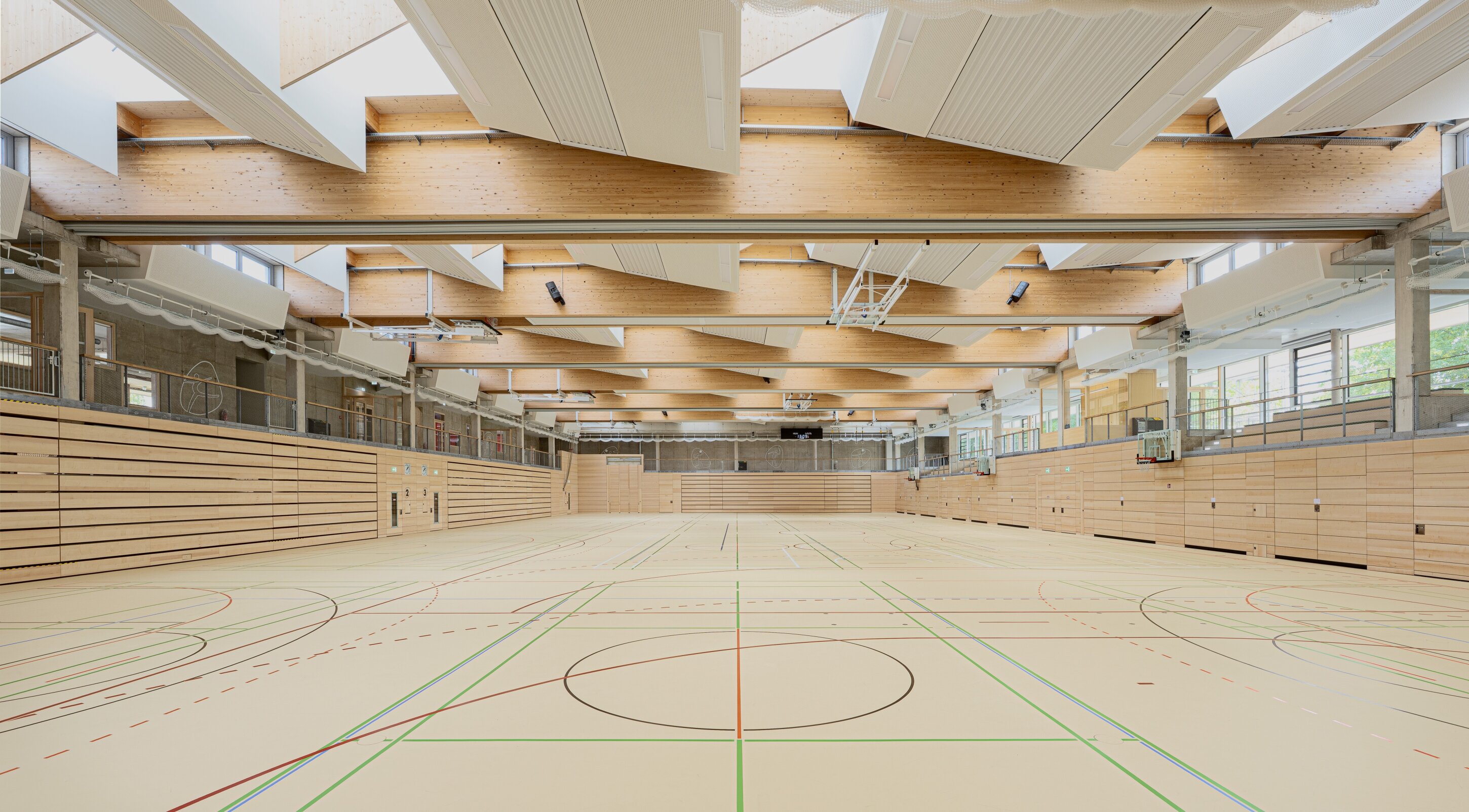 Project by Behnisch Architekturbuero, Family Center R&ouml;thelheim 11acht and Gerd Lohwasser Sports Hall. Empty indoor sports hall with marked courts, wooden wall panels, and a ceiling of exposed beams and acoustic panels.