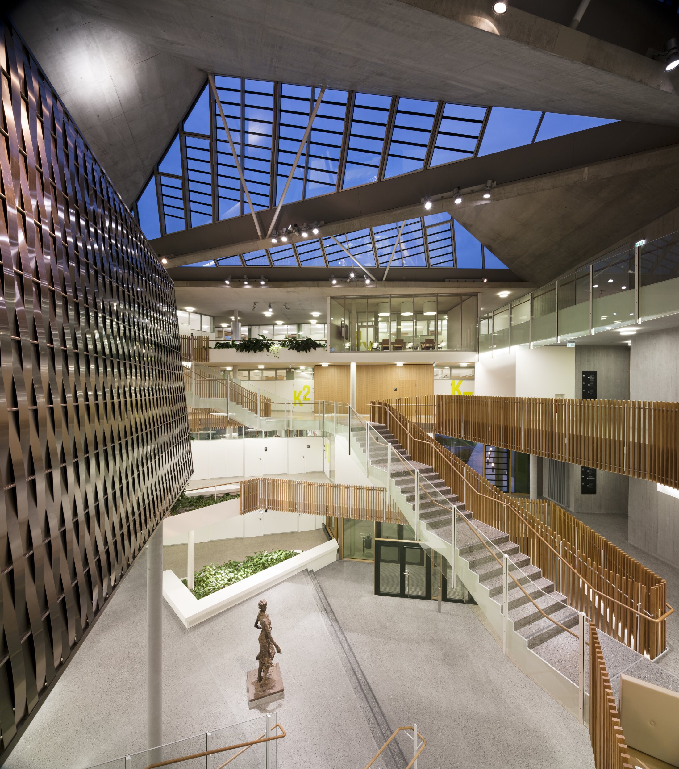 Project by Behnisch Architekturbuero, NCT National Center for Tumour Diseases. Spacious atrium with skylight roof, multiple staircases, glass railings, wood accents, and a sculpture on the ground floor.