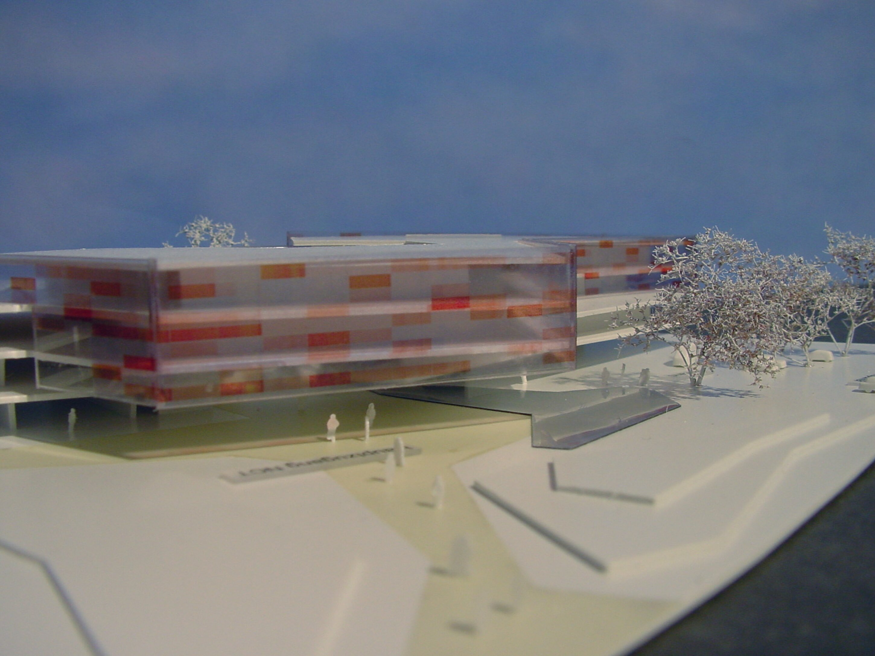 Project by Behnisch Architekturbuero, NCT National Center for Tumour Diseases. Architectural model of a long, low building with a translucent facade, small figures, paths, and trees arranged on a site base.