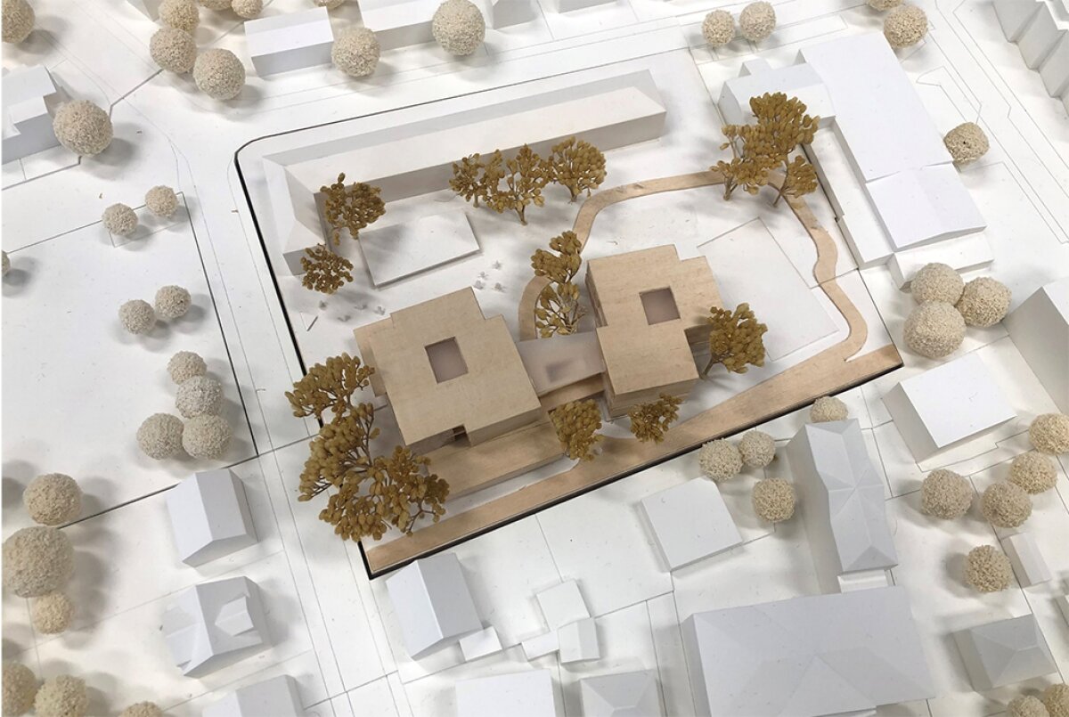 Project by Behnisch Architekturbuero, Elementary school Bad Neuenahr. Top view of an architectural model with two square buildings, surrounding trees, paths, and neighboring structures in a simplified white layout.