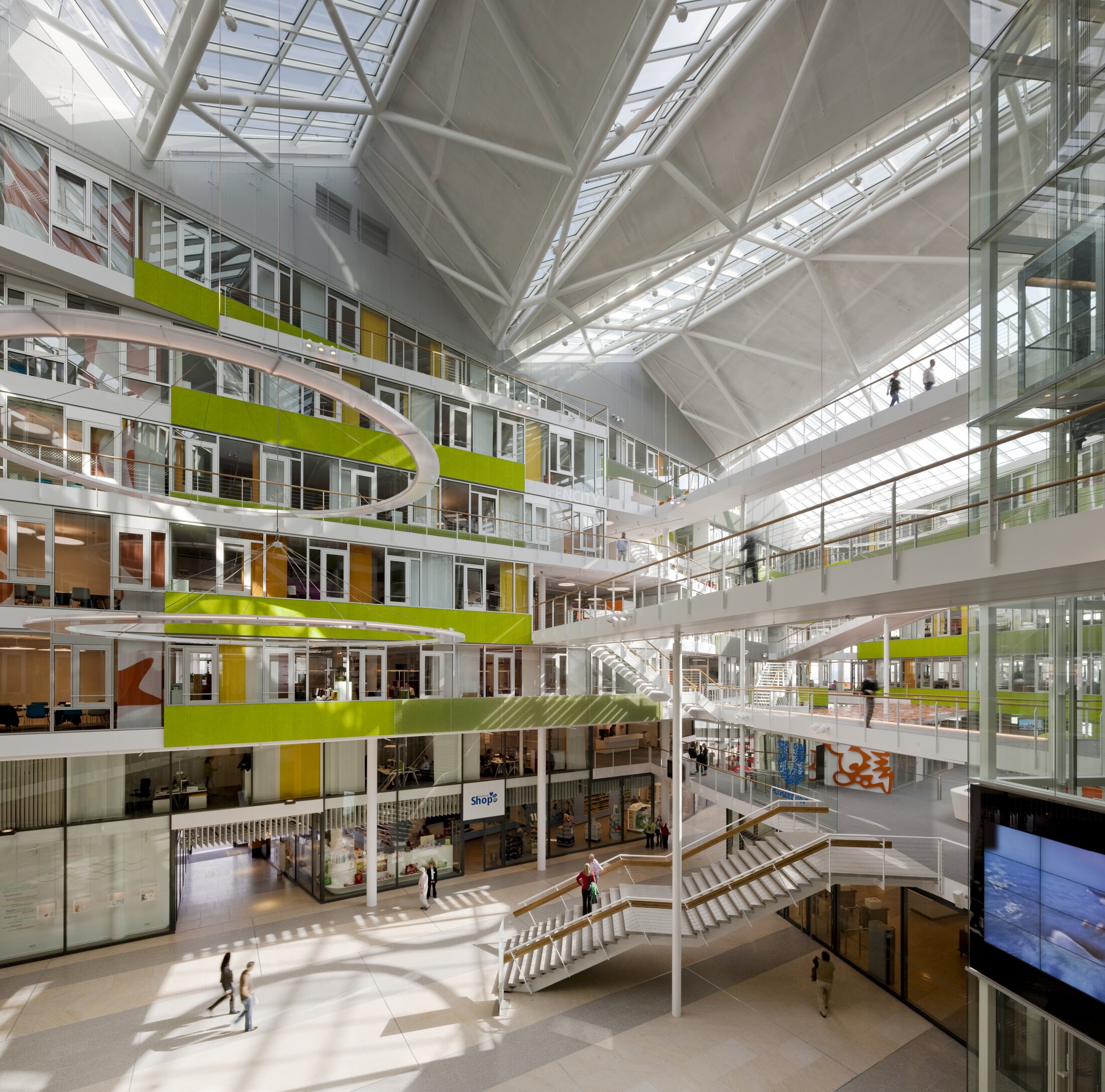Project by Behnisch Architekturbuero, Unilever Headquarters for Germany, Austria, and Switzerland. Large multi-story atrium with glass roof, green-accented balconies, staircases, and people walking across open interior walkways.