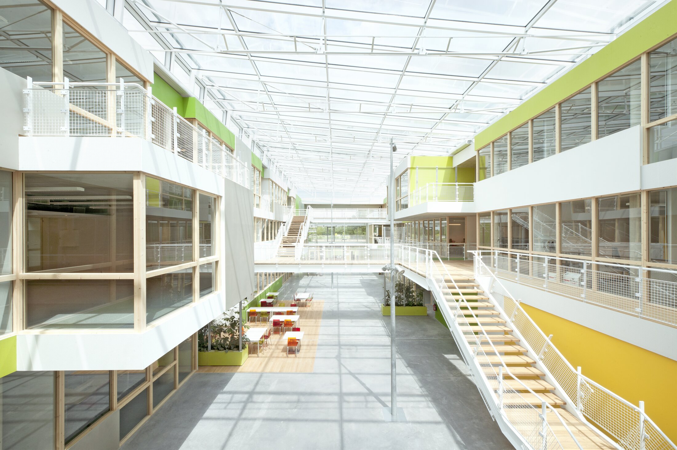 Project by Behnisch Architekturbuero, Digiteo Labs - 3 Research Buildings. Bright atrium with glass roof and green-accented offices, connected by walkways and railings around an open central space.