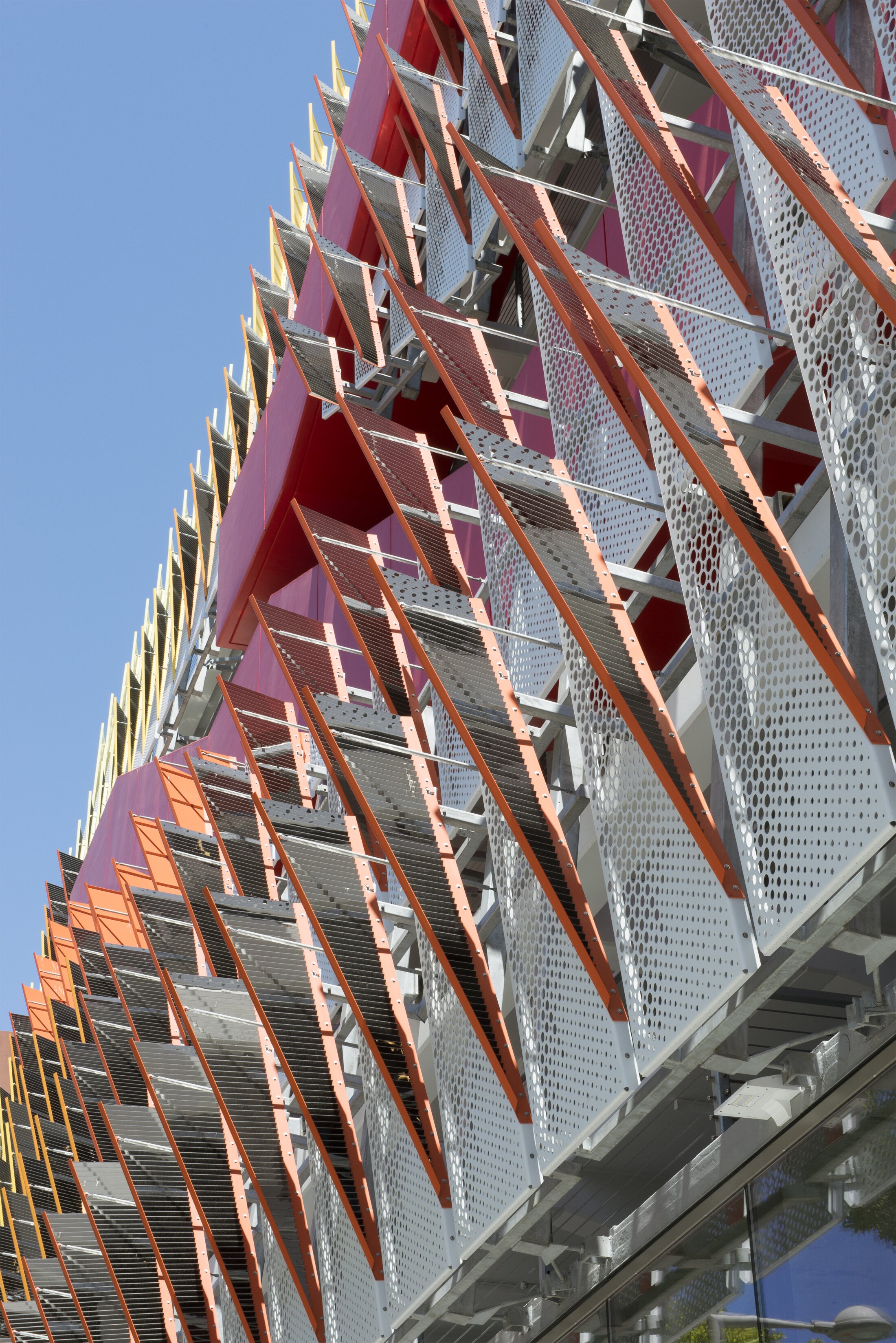 Project by Behnisch Architekturbuero, City of Santa Monica Parking Structure #6. Close-up of the parking garage facade from below. It contains colors such as red, yellow, orange, and white.