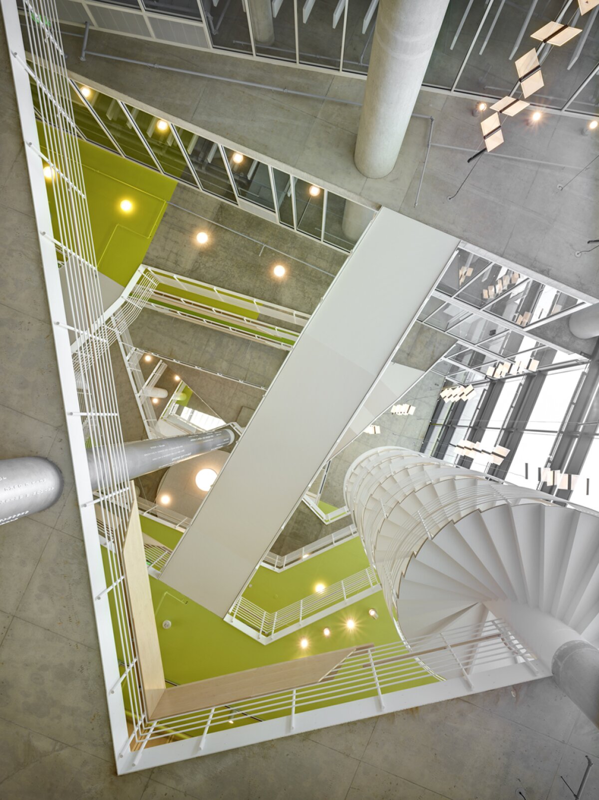 Project by Behnisch Architekturbuero, The John and Frances Angelos Law Center. Top view of a multi-story atrium with green floors, white railings, bridges, columns and a spiral staircase connecting the levels.