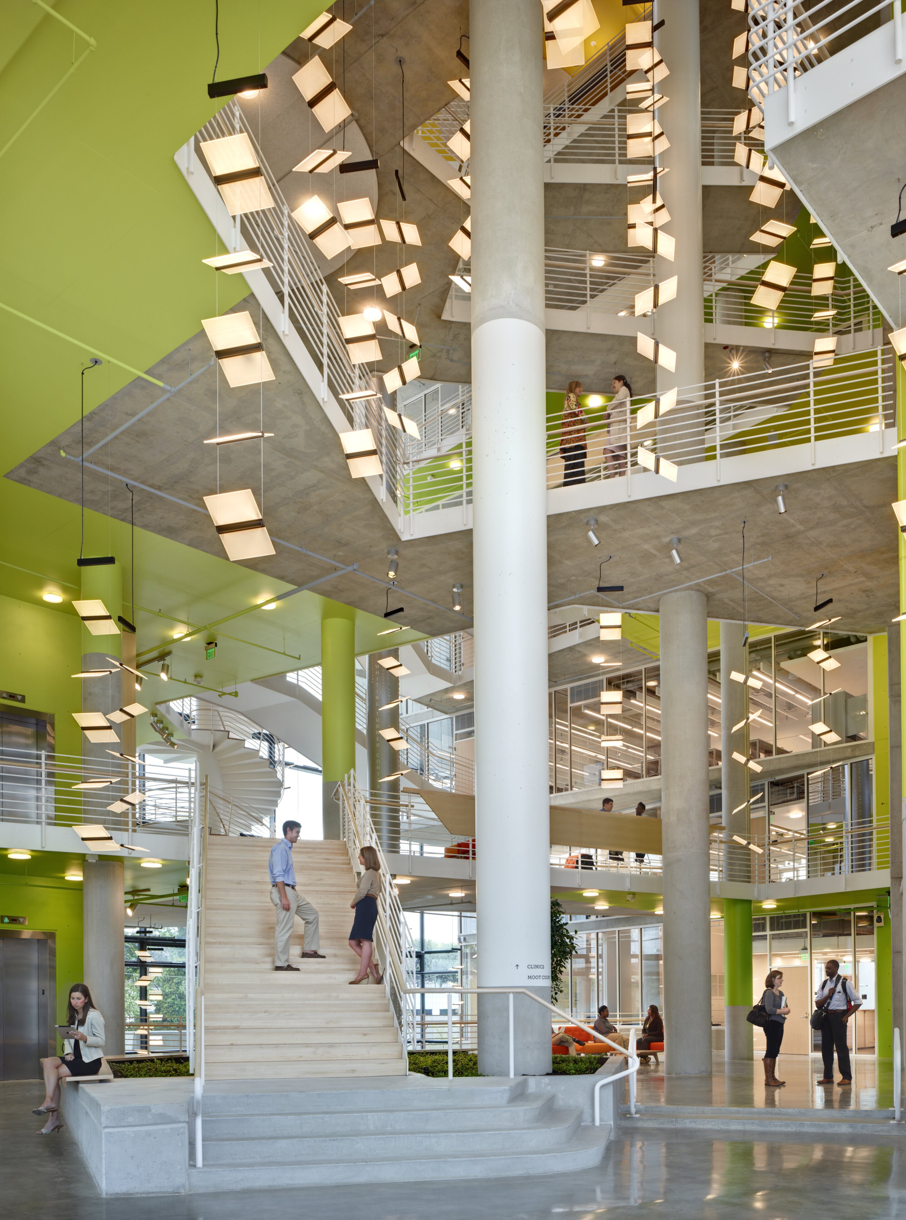 Project by Behnisch Architekturbuero, The John and Frances Angelos Law Center. A multi-story atrium with staircases, white railings, columns, and hanging lights. People stand, walk, and converse in the open interior spaces.
