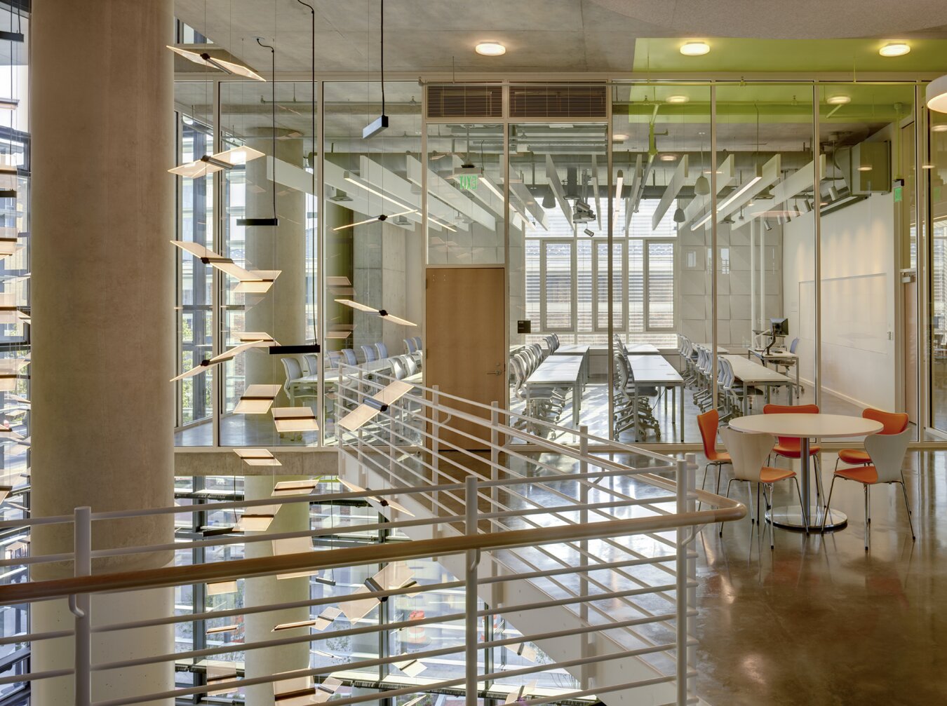 Project by Behnisch Architekturbuero, The John and Frances Angelos Law Center. Interior balcony with metal railing, hanging light panels, and glass-walled classroom beyond. Tables and chairs arranged in a bright modern space.
