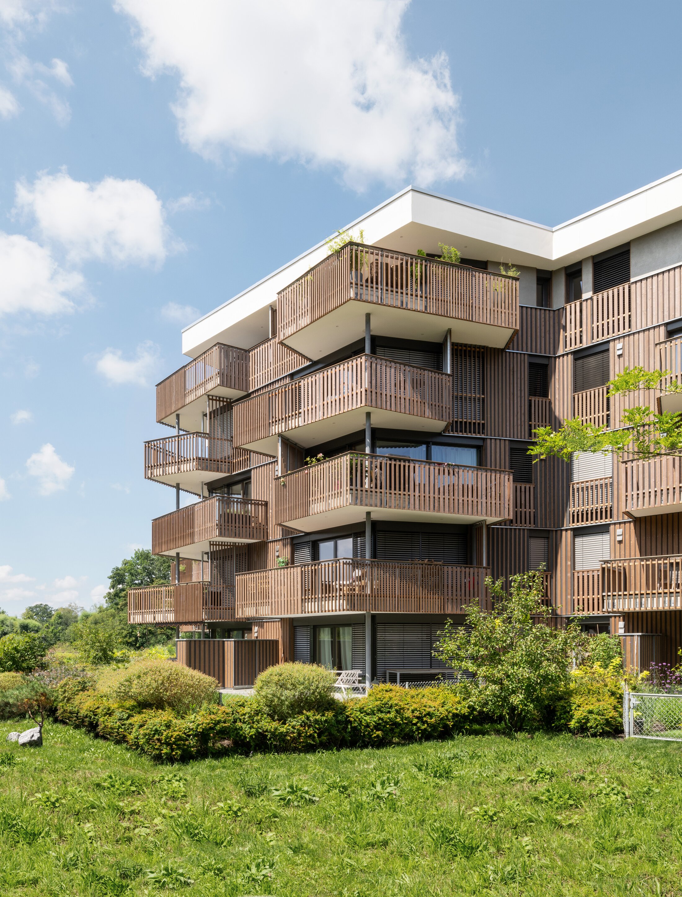Project by Behnisch Architekturbuero, Conradty-Houses. Modern apartment building with staggered balconies and vertical wood facade panels. The varying densities in the wooden balustrades produce  variations in privacy and openness.