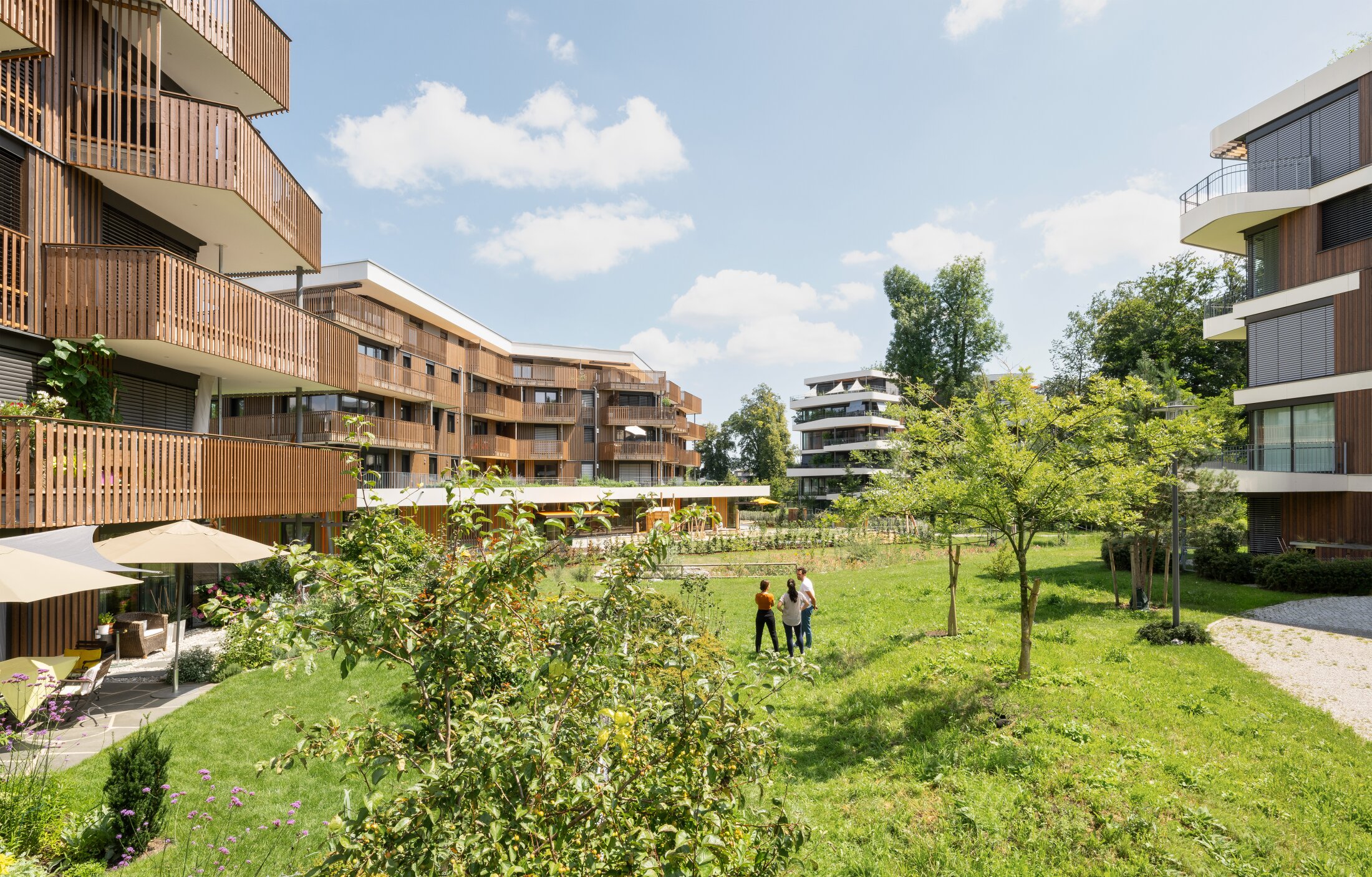 Project by Behnisch Architekturbuero, Conradty-Houses. Multi-story residential buildings with a wooden facade and wooden balconies around a shared green courtyard with trees.