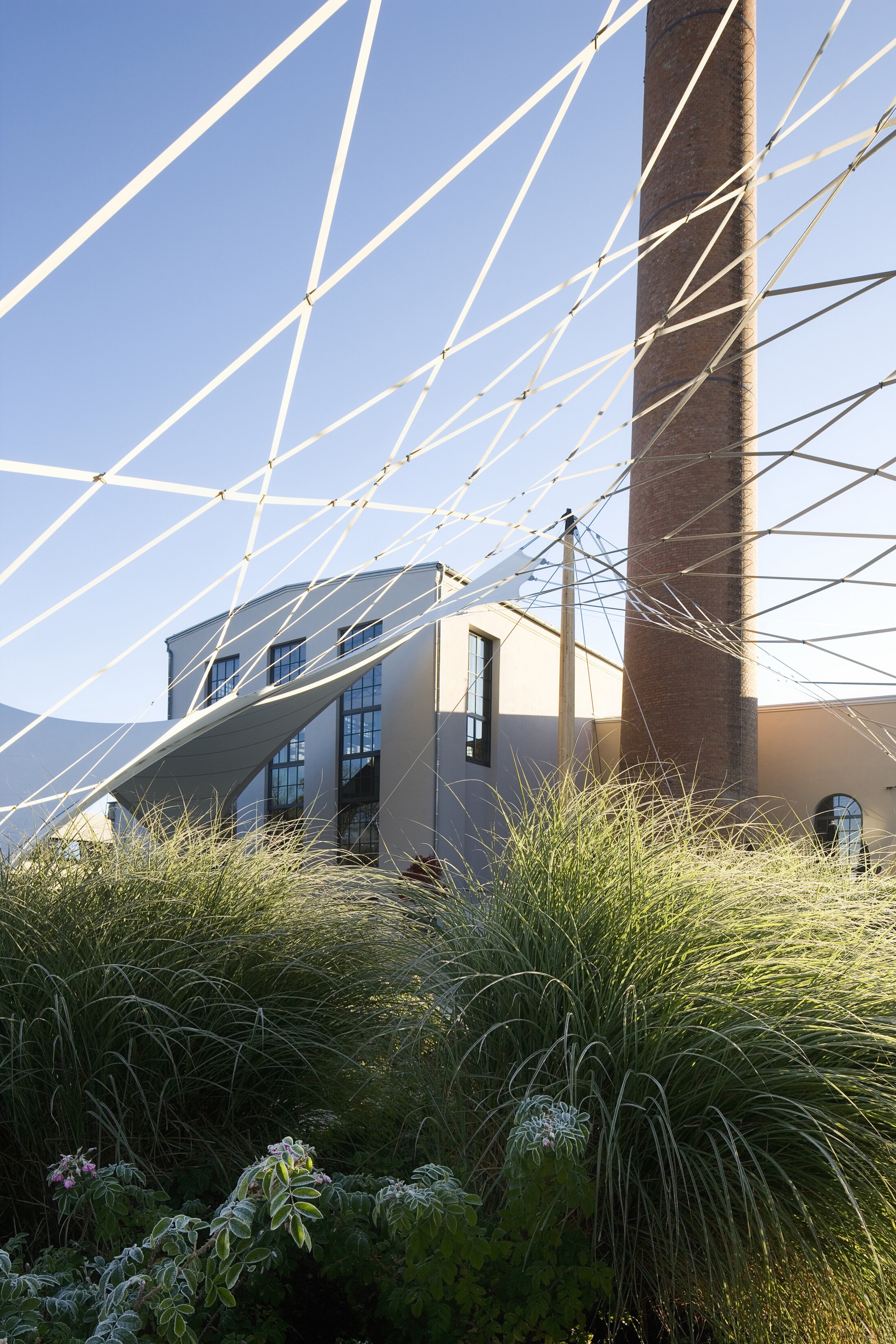 Project by Behnisch Architekturbuero, Boiler House and Rosengarten. A white, rope-like net structure is located in the background, behind the boiler house. In the foreground is the rose garden.