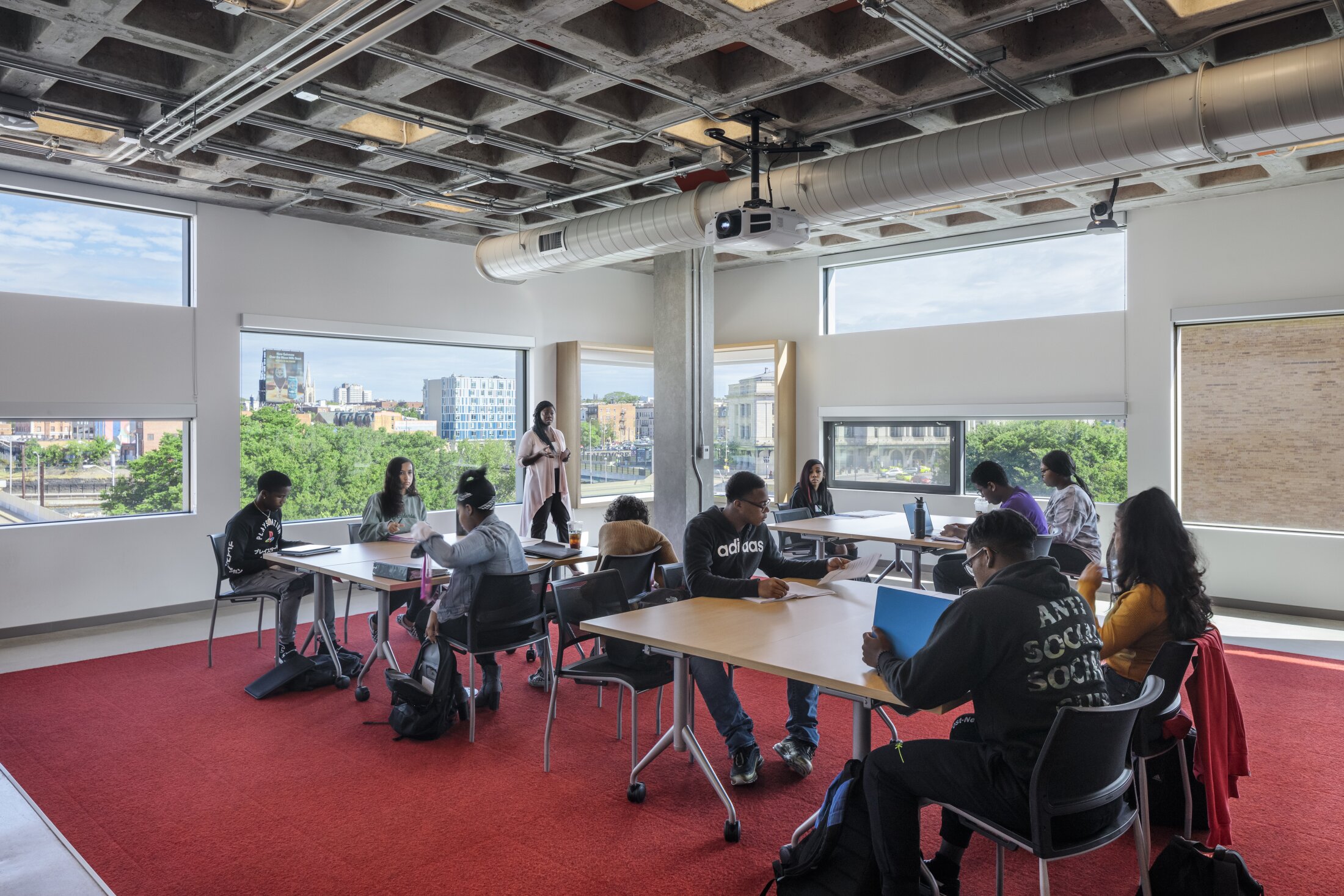 Project by Behnisch Architekturbuero, Robert Bogomolny Library. Students seated at tables in a classroom with large windows and exposed ceiling, reading and discussing while an instructor stands nearby.