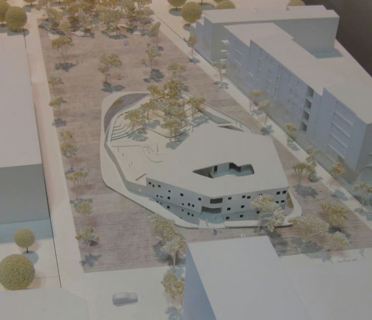 Project by Behnisch Architekturbuero, Townhall Heidelberg Schwetzinger Terasse. Scale model of an irregular-shaped building within a plaza, surrounded by trees, paths, and neighboring block structures.