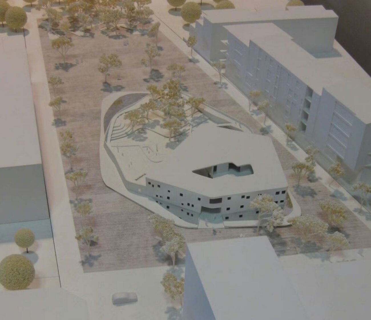 Project by Behnisch Architekturbuero, Townhall Heidelberg Schwetzinger Terasse. Scale model of an irregular-shaped building within a plaza, surrounded by trees, paths, and neighboring block structures.